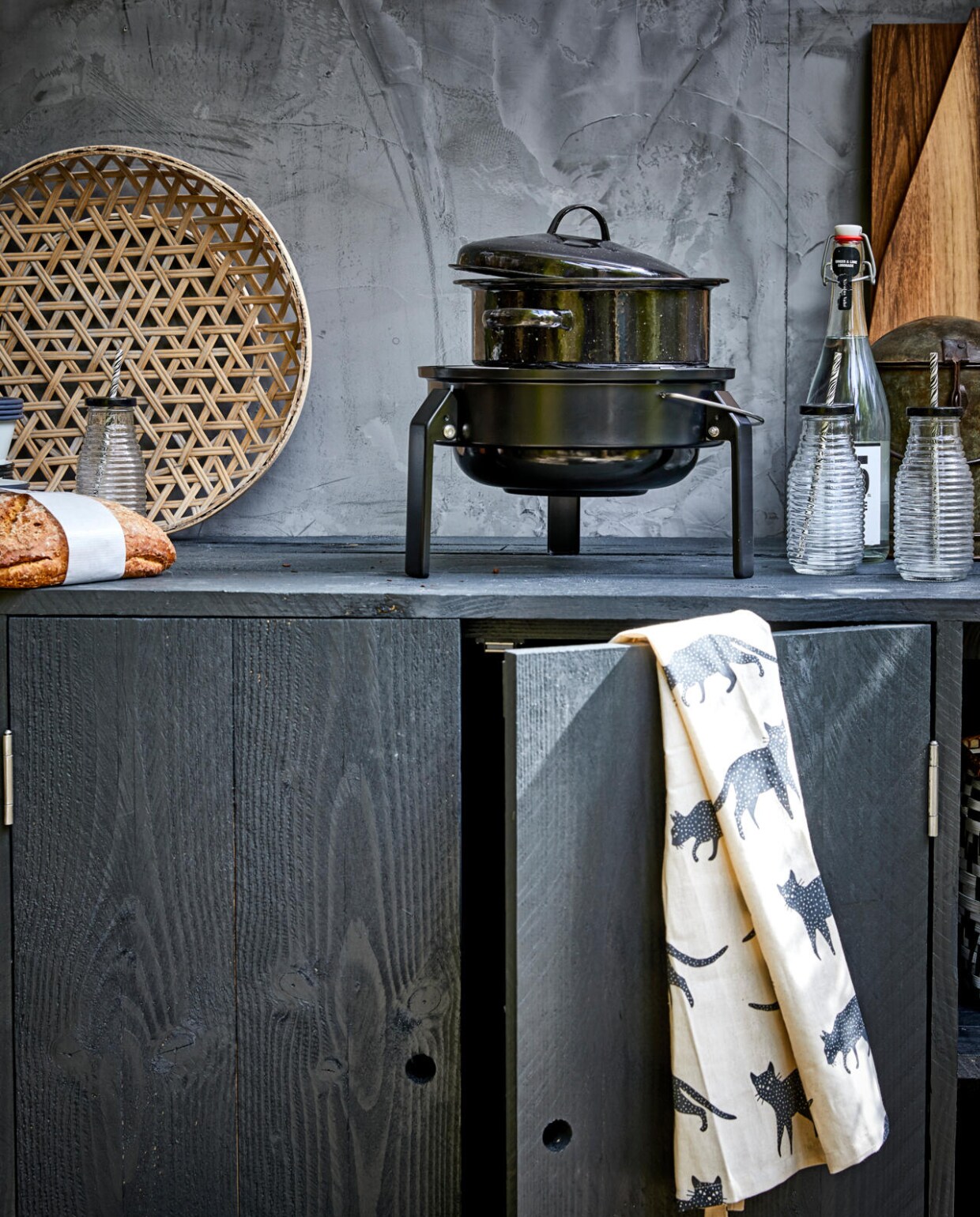 Grote zwarte emaille pan (Madam Stoltz). Flesjes met zwarte dop en rietje (Nordal). Schort (H&amp;M Home). Gevlochten schaal (HK Living). Barbecue Korpön (Ikea). Overig privébezit. vtwonen 2017-07 | styling Cleo Scheulderman | fotografie Jeroen van der Spek