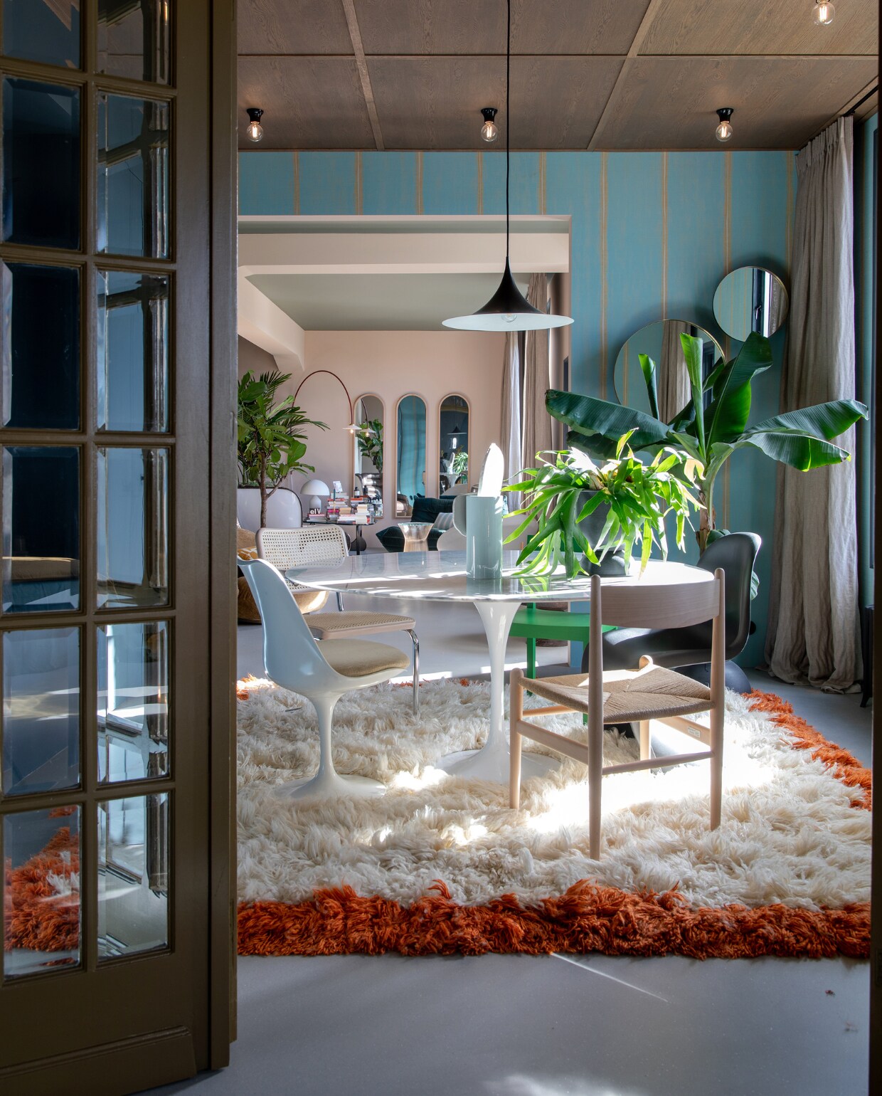 Plafond op maat gemaakt door interieurbouwer Woodever, hanglamp Gubi, bakelieten plafondlampjes Fonq. Behang Elitis via Selected Wallpaper, gordijnen Holland Haag, spiegels Menu. Zwarte stoel Panton van Vitra, houten Carl Hansen-stoel  Berden, witte stoel Tulip van Eero Saarinen, groene stoel Valerie Objects, rotan stoel Thonet. Vloerkleed HKliving, eettafel en harmonicadeur vintage. vtwonen 05-2023 | styling en fotografie Theo-Bert Pot, Jelle van de Schoor