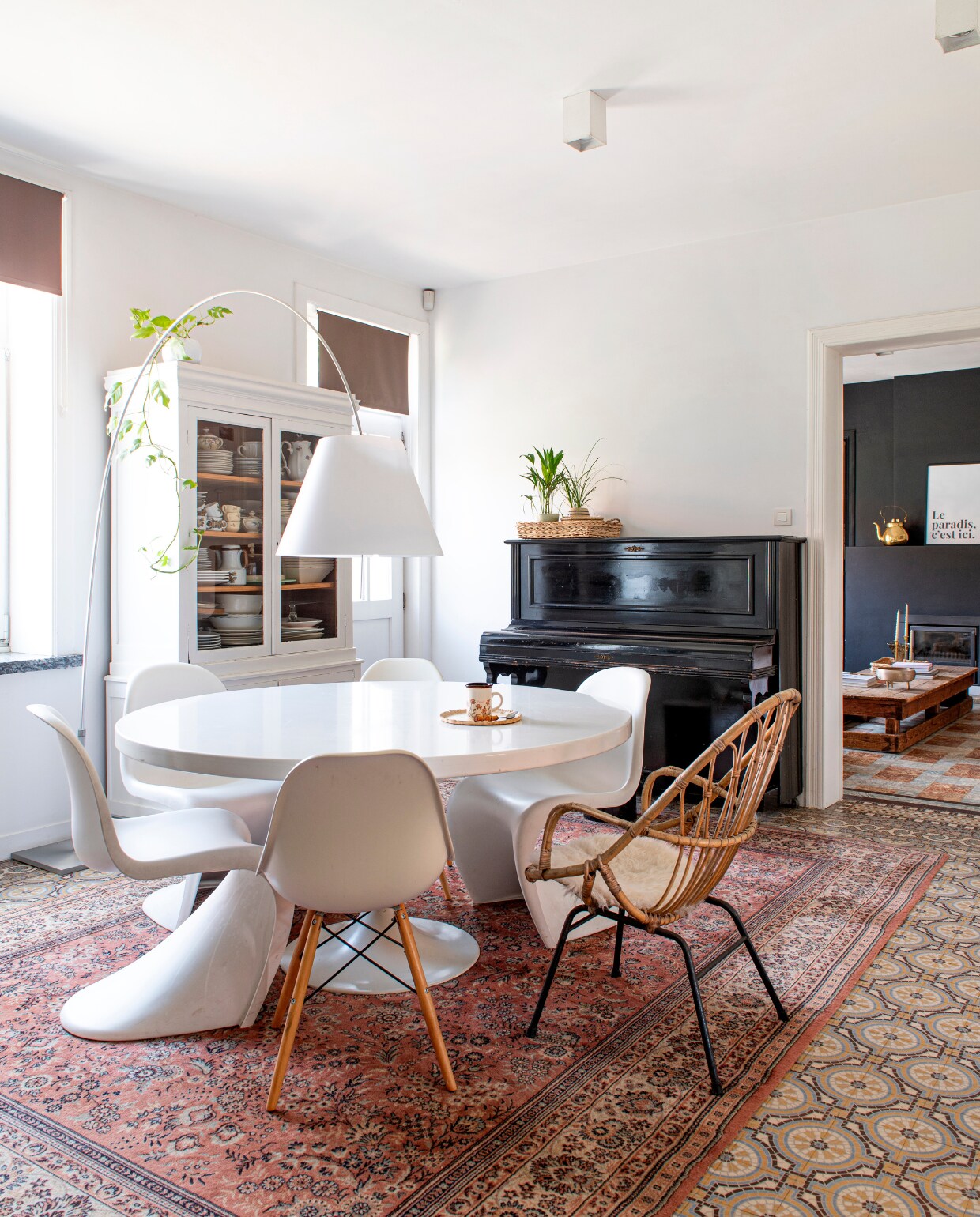 Booglamp Lady Costanza van Luceplan, tafel Tulip van Knoll gekregen van oma, witte plastic stoelen Panton en kuipstoel met houten poten Eames DAW van Vitra, vitrinekast beschilderd erfstuk, rotan stoel Rohé, piano, servies en vloerkleed kringloopwinkel. vtwonen 06-2023 | productie De Binnenkijkers | styling Jeske Weel | fotografie Caroline Coehorst