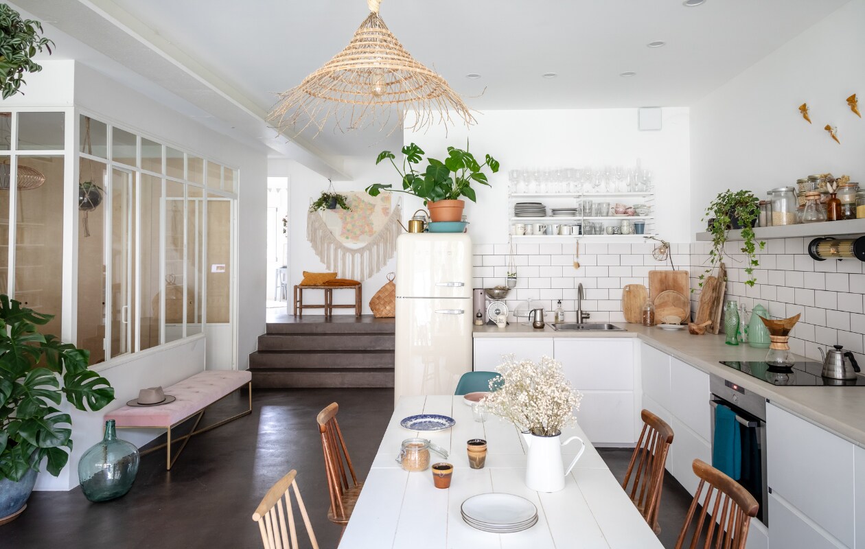 De betonnen vloer is gepolijst. Tafel van Am.Pm (laredoute.com). De donkere houten stoelen zijn tweedehands vondsten van een trip door Normandië. Blauwe Eames stoelen van Vitra, geelgroene stoel van Calligaris (calligaris.com). De keuken is op maat gemaakt met Ikea elementen. Tegels Crédense van Leroy Merlin. Het werkblad is van hout met een laag gewaxte beton van Mercadier (mercadier.fr). Haken van Jungle by Jungle. Manden meegenomen van reizen. Dadelboomblad plafondlamp van Rock the Kasbah (rockthekasbah.net). vtwonen 02-2020 | styling Anne-Catherine Scoffoni | productie Marie-Maud Levron | fotografie Cecile Perrinet-Lhermitte