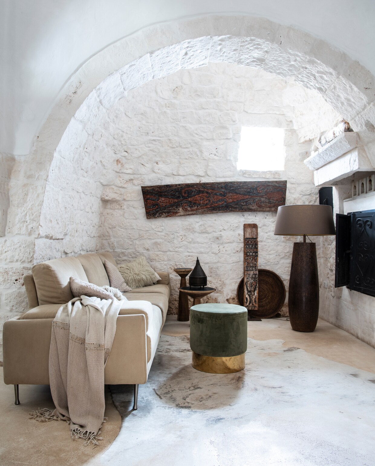 Bank Artifort. Plaid, kussens en rieten dienblad Zara Home. Cementvloer in beige van Calò Lenoci in Ceglie Messapica. Braziliaans koeienvel, poef en bijzettafels Versmissen. Lamp Gert Snel Interiors. Kunstwerk aan de muur en dakspant van Toraja-huis op sokkel souvenirs uit Sulawesi. vtwonen special binnenkijken 06-2022 | productie Insidehomepage | styling Marit Saladini Platjouw | fotografie Louis Lemaire