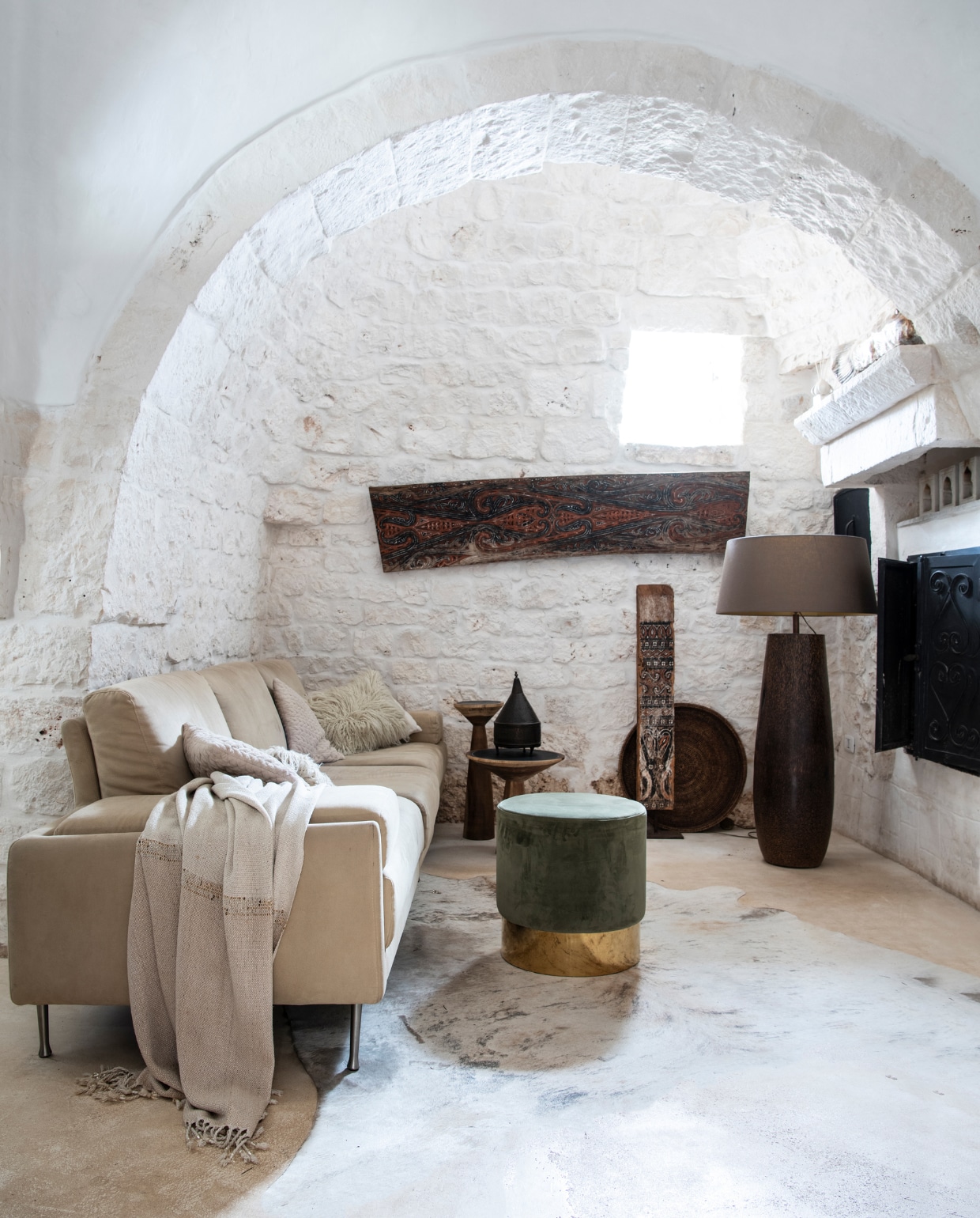 Bank Artifort. Plaid, kussens en rieten dienblad Zara Home. Cementvloer in beige van Calò Lenoci in Ceglie Messapica. Braziliaans koeienvel, poef en bijzettafels Versmissen. Lamp Gert Snel Interiors. Kunstwerk aan de muur en dakspant van Toraja-huis op sokkel souvenirs uit Sulawesi. vtwonen special binnenkijken 06-2022 | productie Insidehomepage | styling Marit Saladini Platjouw | fotografie Louis Lemaire | tekst Inge van Lieshout | | tekstbewerking Merel van der Lande