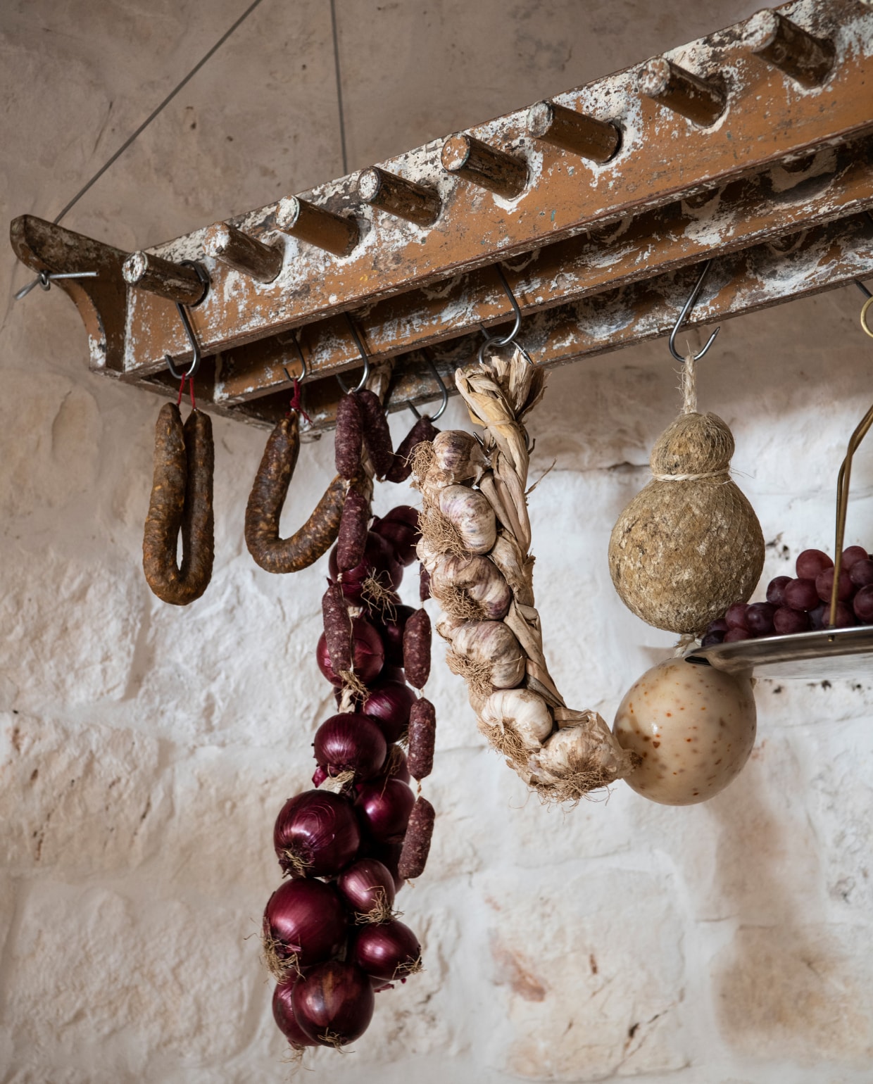 Het keukenrek is een oude klossenplank uit een Indiase textielfabriek. Aan de S-haken: uien, knoflook en Caciocavallo di Martina Franca (kaas). vtwonen special binnenkijken 06-2022 | productie Insidehomepage | styling Marit Saladini Platjouw | fotografie Louis Lemaire