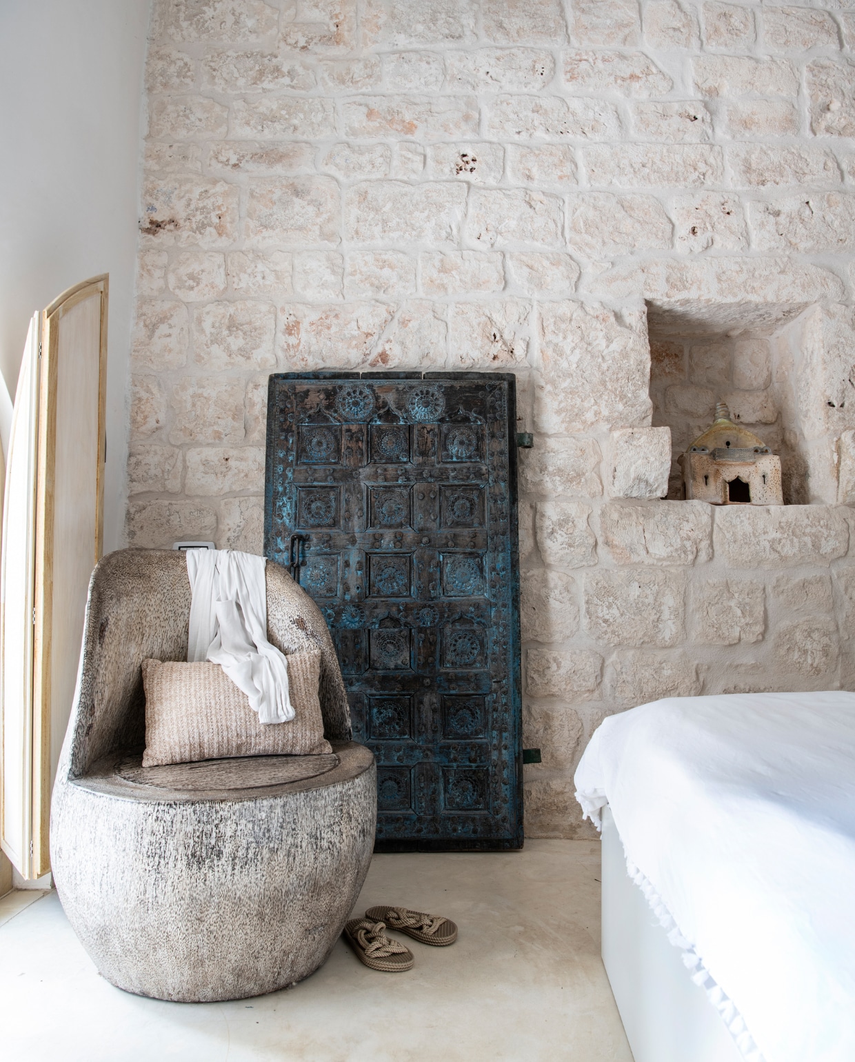 Palmhouten stoel uit Indonesië en Indiase staldeur met houtsnijwerk Gert Snel Interiors. Kussen Zara Home. Slippers Zara. Luik gemaakt door lokale timmerman. Keramieken beeld in nis is gemaakt door Nicoles moeder. vtwonen special binnenkijken 06-2022 | productie Insidehomepage | styling Marit Saladini Platjouw | fotografie Louis Lemaire