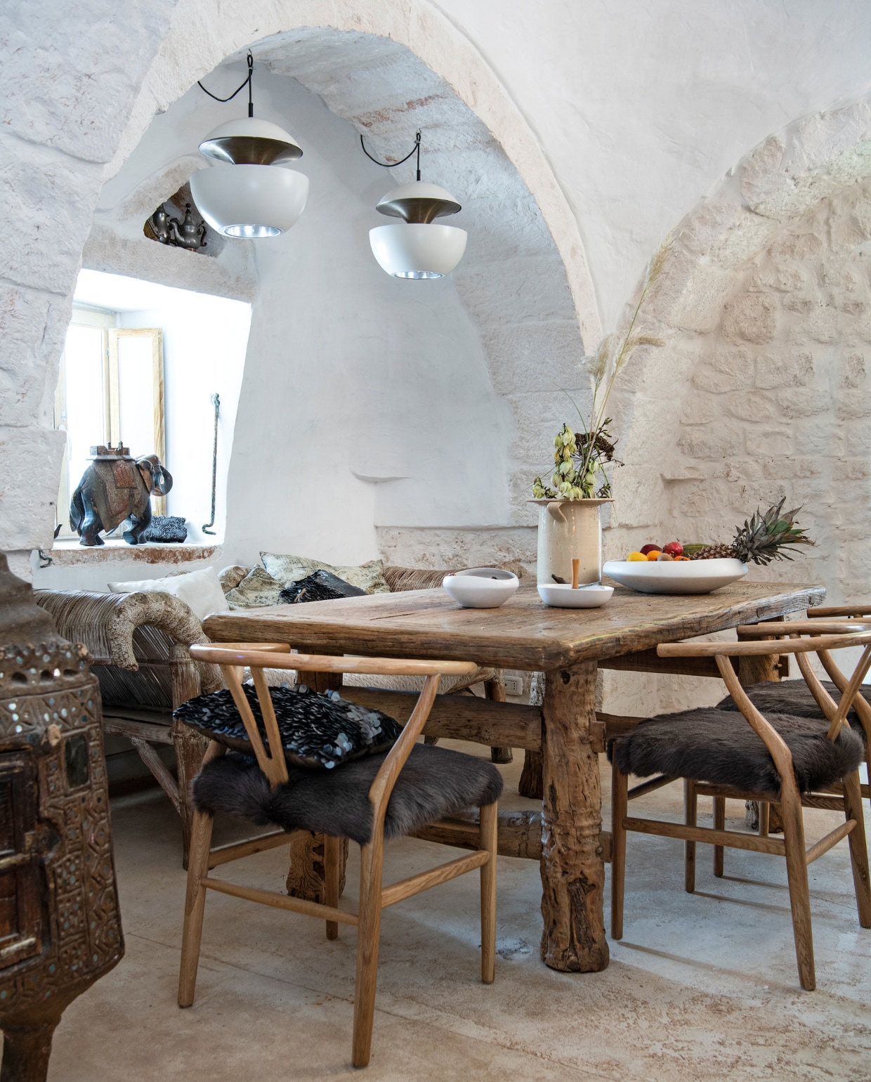 Chinese iepen-houten eettafel. Wishbone-stoelen Gert Snel Interiors. Zwart paillettenkussen PTMD. Palmhouten loungebank en oude struisvogelei-broedmachine (links) uit Indonesië. Retro hanglampen Raak. Aardewerken vaas antiekmarkt Ostuni. Fruitschaal Now’s Home. Schaaltje met houten handvat Yong. In de nis: twee Toeareg-theepotjes. Overig onbekend. vtwonen special binnenkijken 06-2022 | productie Insidehomepage | styling Marit Saladini Platjouw | fotografie Louis Lemaire