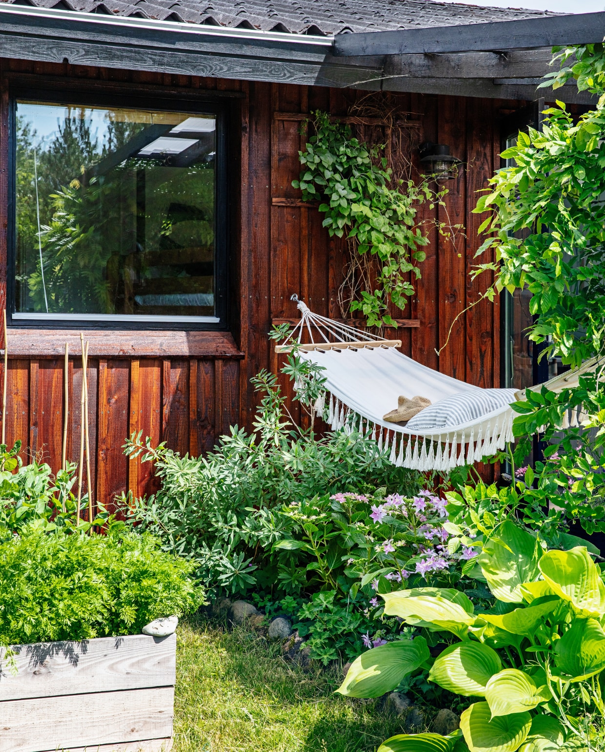 De hangmat van de Deense supermarkt Rema tussen de blauweregen en vlinderstruiken. vtwonen special binnenkijken 06-2022 | productie Living Inside | styling Rikke Graff Juel | fotografie Christina Kayser O.