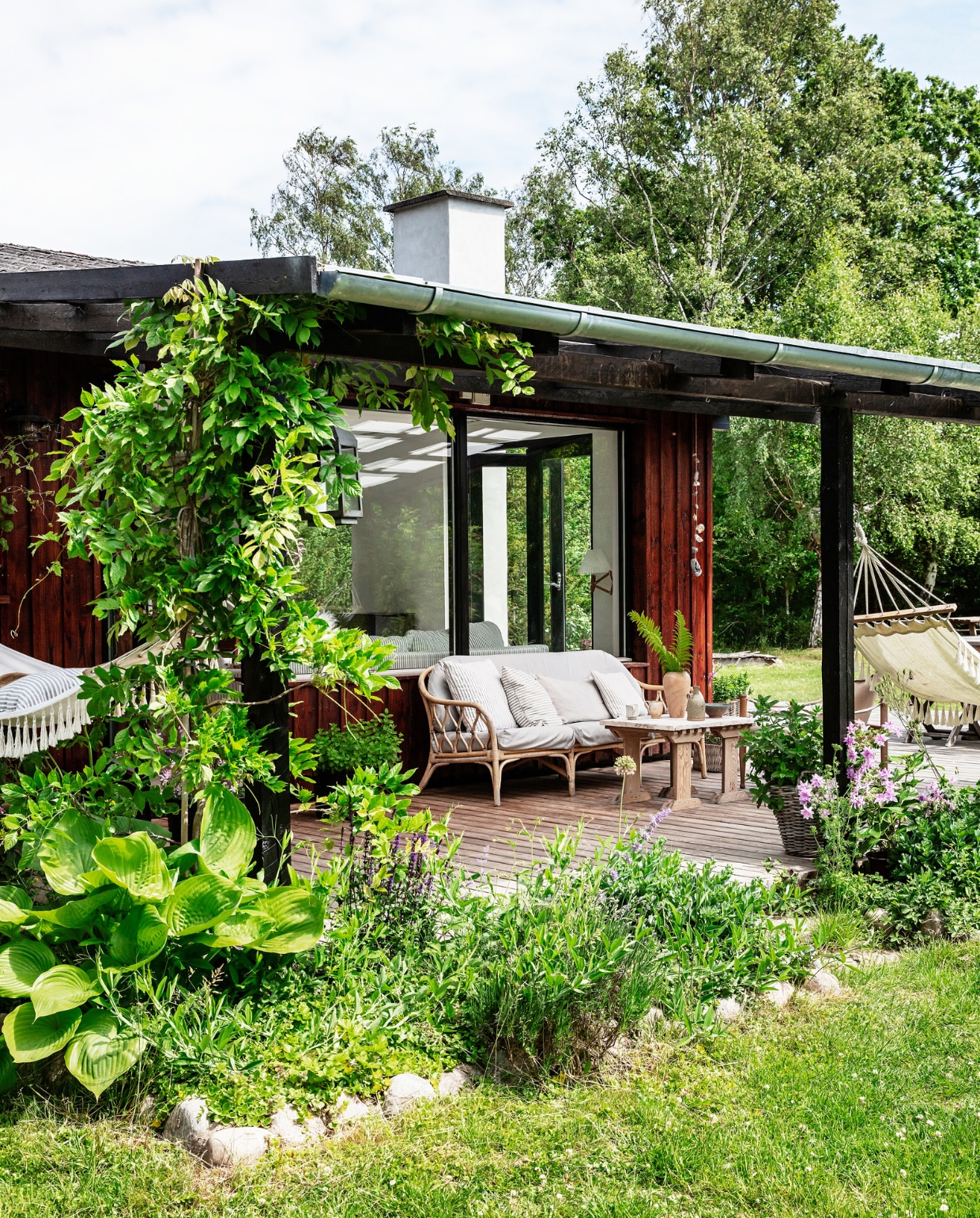 Het hele huis is omringd door een terras met overal zitjes. Bamboebank vintage. vtwonen special binnenkijken 06-2022 | productie Living Inside | styling Rikke Graff Juel | fotografie Christina Kayser O.