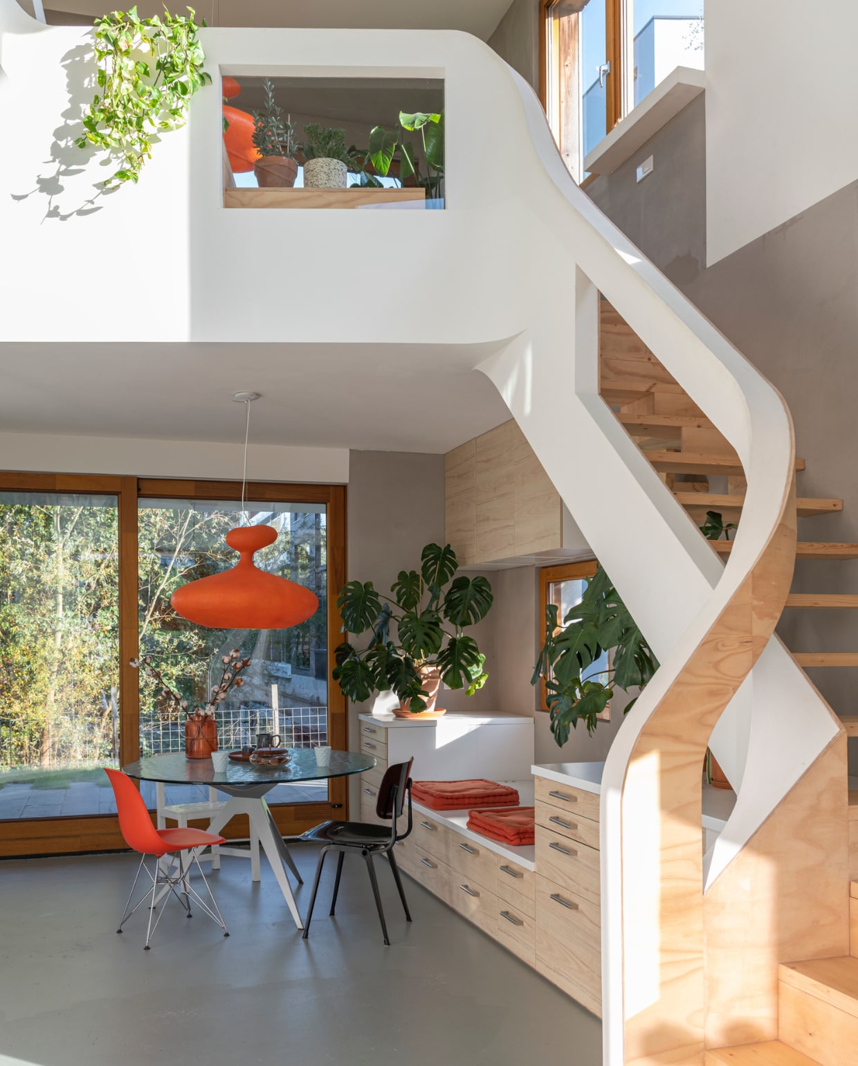 Zandcementdekvloer met vloercoating, trap en houten muren van vurenhout en radiplex, eettafel Ben Hoek Meubelarchitectuur, lamp Kundalini E.T.A. Sat, oranje stoel Charles Ray Eames, zwarte stoel Revolt van Friso Kramer, witte stoel Joep van Lieshout, oranje vaas Kwantum, dienblad H&M Home, kan Søstrene Grene, lichtblauwe mokken kringloop, koektrommel met houten deksel en grijze aardewerken pot vintage, oranje palletkussens tuincentrum, terracotta potten Intratuin en Ikea, handgrepen lades Ikea. vtwonen 01-2021 | productie & fotografie Caroline Martinot | styling Sharon Roest