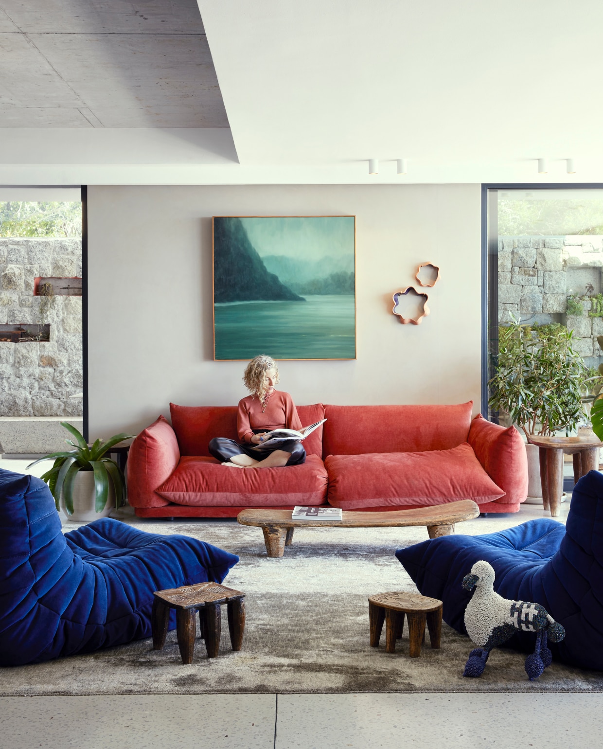 Bank Wunders. Blauwe fauteuils Ligne Roset. Vloerkleed Gonsenhausers. Authentieke Senufo-voetenbankjes en -tafels lokaal gekocht. Kralenpoedel Monkeybiz. Schilderij Jake Aikman. Keramische wandkunst gemaakt door Martine. vtwonen special binnenkijken 06-2022 | productie Bureaux | styling Sven Alberding | fotografie Elsa Young