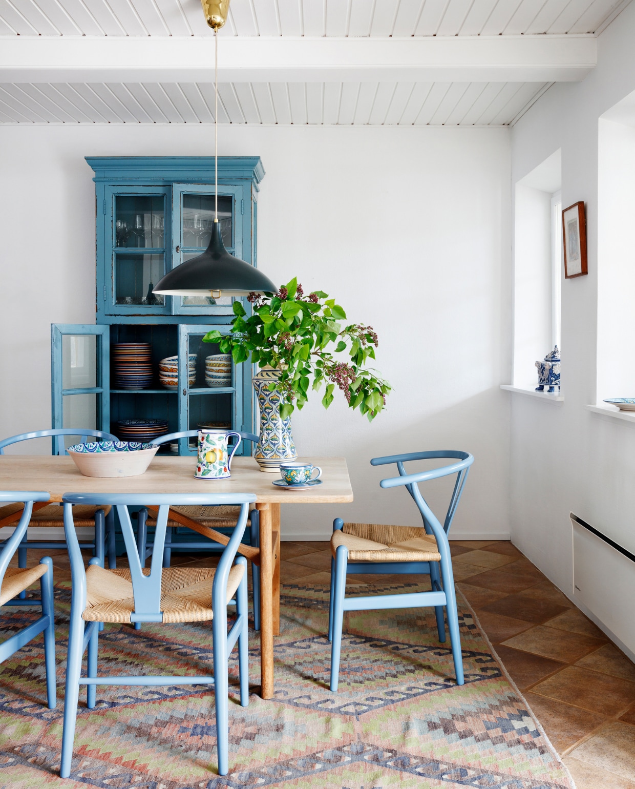 Blauwe kast tweedehands. Stoelen CH24 Wishbone Carl Hansen &amp; Son. Eettafel erfstuk. Lamp Gubi. Servies en vaas Casa Ceramiche. Vloerkleed Noeola. Overig onbekend. vtwonen special binnenkijken 06-2022 | productie Living Inside | styling Rikke Graff Juel | fotografie Christina Kayser O.