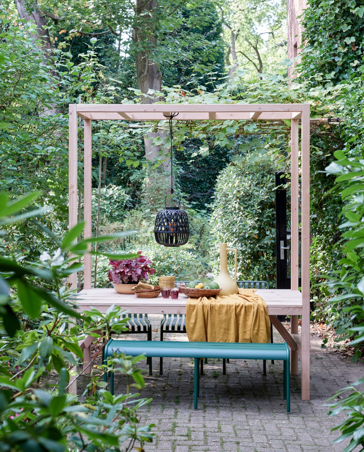 tuinbank Luxembourg van Fermob, stoelen Palisade Chair van Hay (vtwonen.nl). Tafelkleed van okergele stof (patickkarteris.nl). Hoge vaas, diepe borden Glaze (kwantum.nl). Bamboe lantaarn, schaaltjes, schaal (intratuin.nl). Sisal schaal (hm.com). Linnen servetten (hm.com). vtwonen tuin special 5-2022 | diy large | styling Moniek Visser | fotografie Sven Benjamins