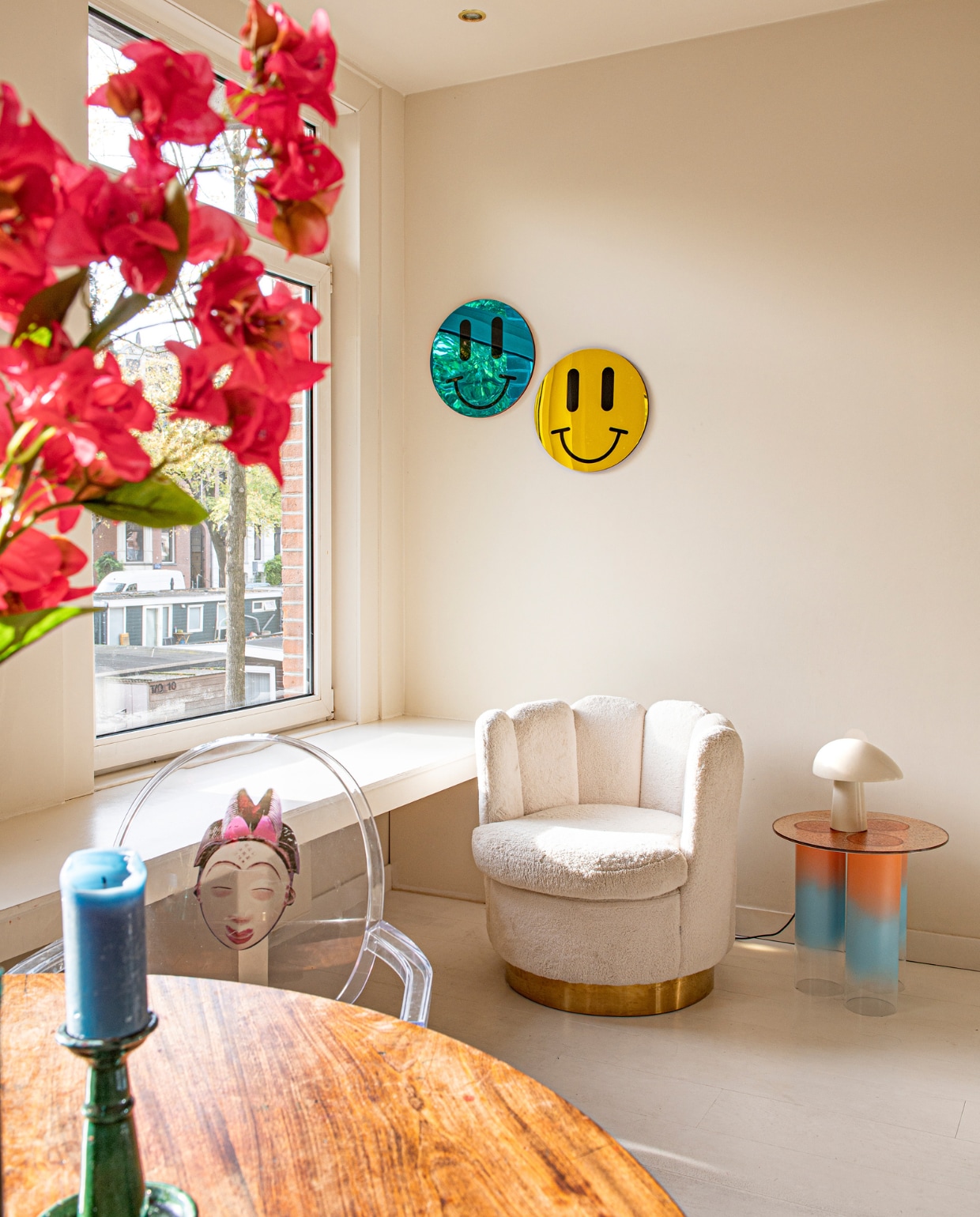 Smiley-spiegels Studio Vacay, stoel Wonenmetlef, bijzettafel Studio Fleur Peters, tafellamp Night Owl van Fritz Hansen, kandelaar Enstijl, stoel Louis Ghost van Kartell, tafel erfstuk. vtwonen 07-2023 | productie De Binnenkijkers | styling Jeske Weel | fotografie Caroline Coehorst