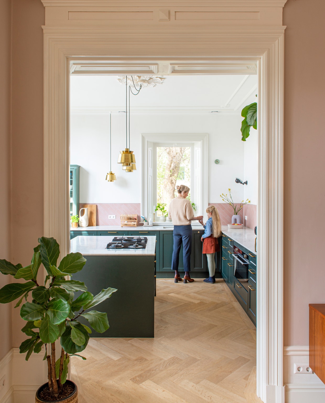 Keukenfronten Noremax, geverfd in Studio Green van Farrow &amp; Ball. Tegels Tegelstore. Hanglampen &amp;Tradition. Wandlampen Jieldé. Gieter Ferm Living. Afdruiprek Dille &amp; Kamille. Klok en roze fruitschaal Studio Harm en Elke. Paarse vaas H&amp;M Home. vtwonen special binnenkijken 03-2023 | productie De Binnenkijkers | styling Jeske Weel | fotografie Caroline Coehorst