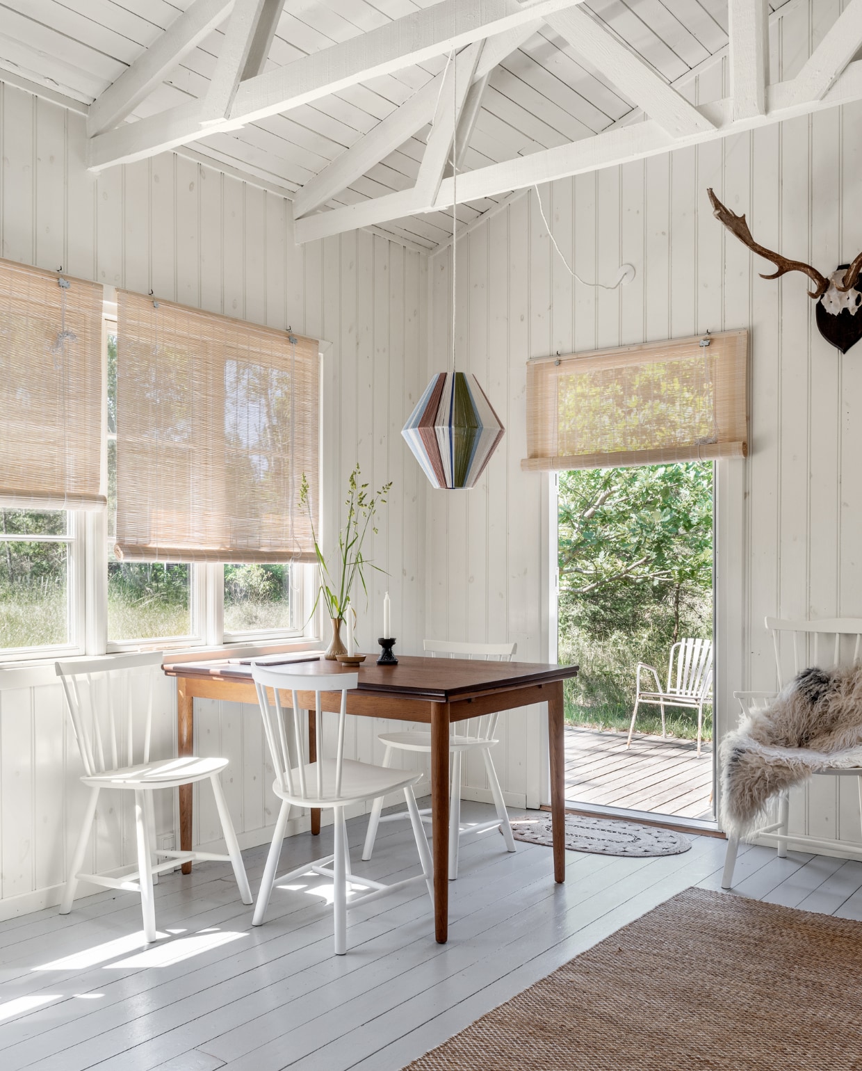 Rieten rolgordijnen Aziatische winkel. Teakhouten tafel, kandelaars en vaas rommelmarkt. Stoelen J46 FDB Møbler. Hanglamp gemaakt door een vriendin. Gewei is afkomstig van Rikke,s vader. Vloerkleed Hay. Deurmat H&M Home. Schapenvacht gekregen. vtwonen special binnenkijken 06-2022 | productie Living Inside | fotografie Peter Kragballe