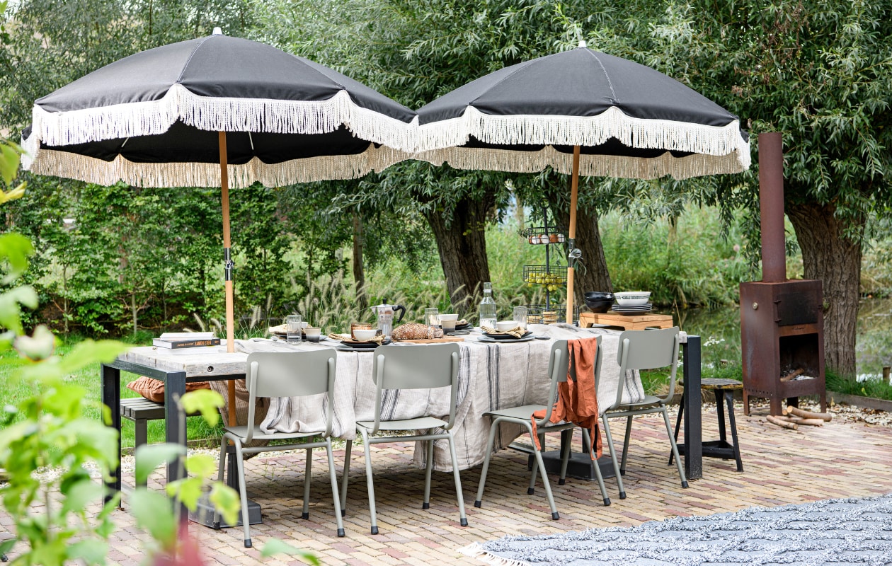 Parasol, per stuk € 159,- (yuna-merch.com). Tuinstoelen Back to School € 219,- (zuiver.com). Vloerkleed Mintras, gemaakt van petflessen, 140x200 cm € 248,-, etagère Conches € 59,95, waterglazen Padiès, set van 6 € 36,95, katoenen kussen op de bank Boclour, set van 2 € 36,95 (loberon.nl). Linnen tafelkleed, 140x220 cm € 95,-, vintage mokken € 6,75, dinerbord Gradiënt Ceramics € 14,95, zwart keramieken dessertbord Kyoto € 6,95, bruin sideplate Bold and Basic, set van 2 € 27,95, rijstkom € 7,95, zwarte kommen op houten plank Bold and Basic, set van 2 € 24,99, geurkaars Porch Night € 34,95 (hkliving.nl). Waterkaraf Sällskaplig € 9,99, borden Strimmig, set van 4 € 14,99, schaal € 3,49 (ikea.com). Schort € 17,99 (sissy-boy.com). Houten tray € 129,-, servetten Cala Llonga € 5,49 (mrsbloom.nl). Pizzaoven van Weltevree € 795,- (fonq.nl). De eettafel en bank zijn ontworpen en gemaakt door Optie A. Overig privébezit. vtwonen tuin special 07 | styling Kim Timmerman | fotografie Louis Lemaire | assistentie Susanne van Schie
