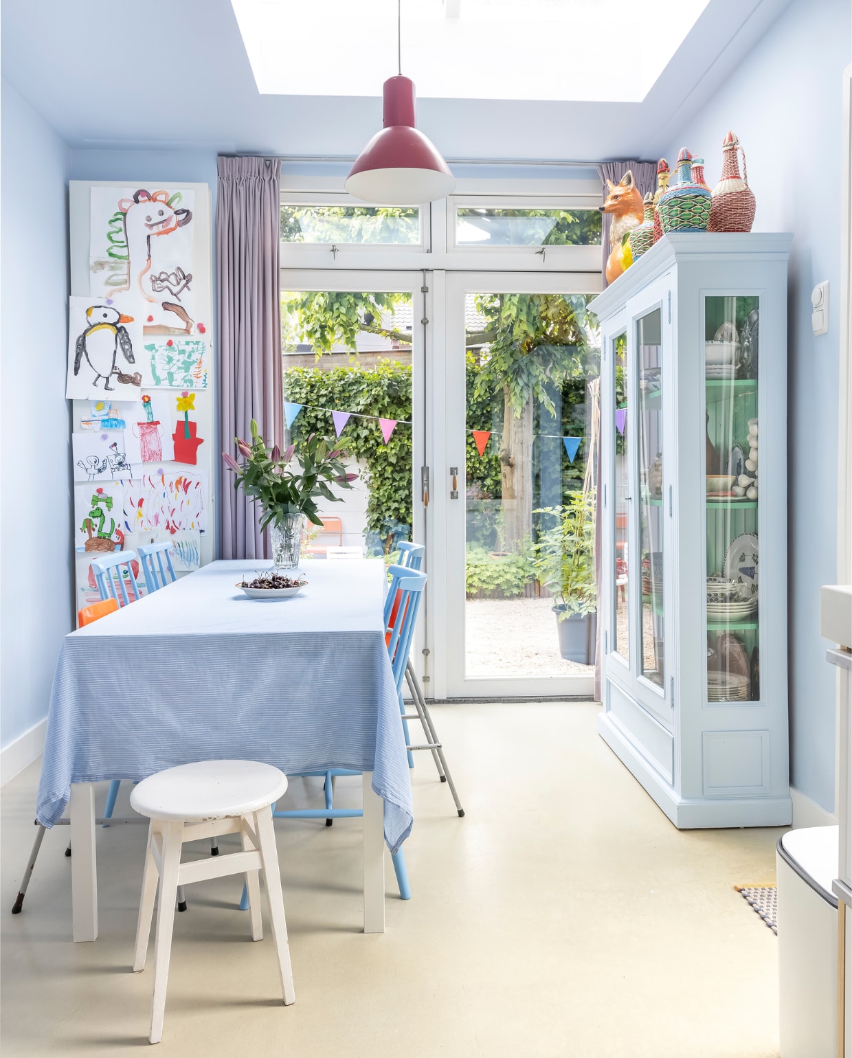 Muur- en plafondverf S2.08.79 van Sikkens, gordijnen Hema, tafel Ikea. Stoelen, kruk, kinderkuipstoelen, rode lamp, object vos, Franse geweven flessen en vaas vintage. Tafelkleed zelfgemaakt. Kast Markplaats, geschilderd in de kleur van de muur. Deurmat Hay, prullenbak Brabantia. Overig onbekend. vtwonen 07-2023 | fotografie Henny van Belkom