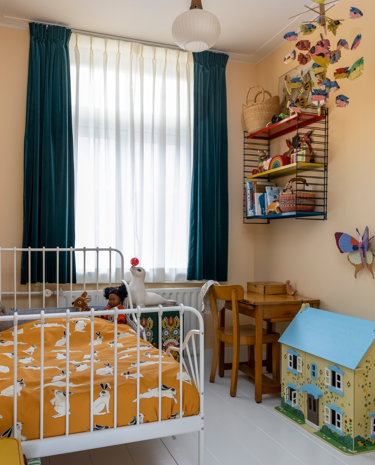 Muurverf E7.18.80 van Sikkens, houten vloer wit geschilderd, vitrage Hema. Velours gordijnen en bed Ikea. Pop Paola Reina, beddengoed Mini Rodini, gestreepte speelgoeddoos Djeco. Lamp, schooltafel, stoel en vissenmobile vintage. Wandrek Tomado, poppenhuis Cottage van Bigjiggs via Marktplaats, zeehondlamp Heico, nachtkastje vintage, muurvlinder Studio Roof. Overig onbekend. vtwonen 07-2023 | fotografie Henny van Belkom