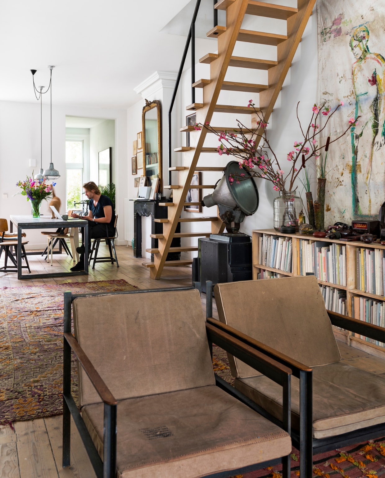 Fauteuils van Loftstyles in Antwerpen. Vloerkleed uit India, tafel uit Bali, lampen van een vintage markt. De kast voor alle kunstboeken is een eigen ontwerp en afgestemd op de maat van het grootste boek. Achter de kast een doek van Jasper. Onder de trap staat een stadionlamp op een mal van de Nederlandse Spoorwegen. Het hekwerk naast de trap is gemaakt door Fraai Metaal, een kunstenaar die met staal werkt. Hij heeft het staal gemoffeld, waardoor het een matte kleur zwart krijgt. vtwonen 10-2016 | styling Emmy van Dantzig | fotografie Stan Koolen