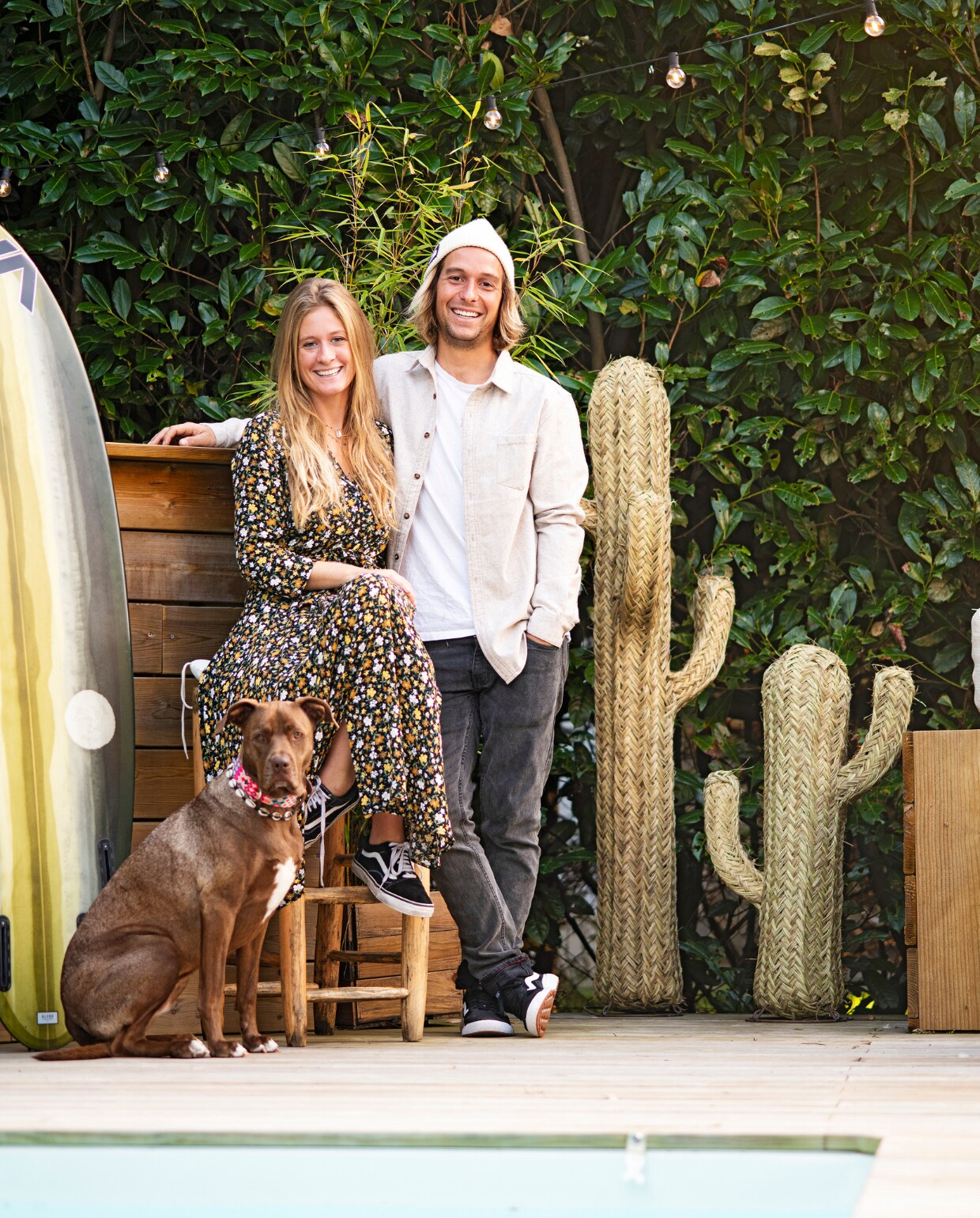 Juliette, Sam en hond Mexie op het terras bij het zwembad. De surfplank werd bewerkt door Blend Glassing Studio. De bar timmerde Sam zelf. Gevlochten cactus Philippine Boho in Hossegor. vtwonen special binnenkijken 06-2021 | productie Anne-Catherine Scoffoni | styling Catherine Cornille | fotografie Patrick Sordoillet