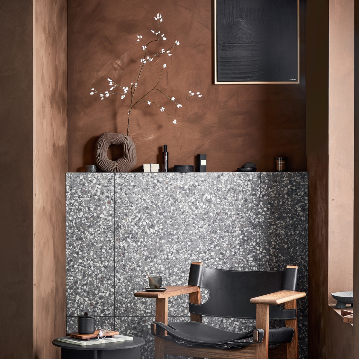 Vloer- en wandtegels Terrazzo Lead Flakes, 90x90 cm per m² € 78,-.M.m.v. vestingh.nl (muurverf Lab Paint in Holy Monkey), designtales.nl (fauteuil van Fredericia), vtwonen.nl (bijzettafel van Hay), boketo.art (kunstwerk), zarahome.com (houten dienblad, zwarte aardewerken pot, onderzetter, zwarte houten schaal), hm.com (aardewerken vaas, glazen bak, ronde houten doos, bruine geurkaars, vierkante houten bak, zwarte aardewerken schaal op poten, houten dienblad in organische vorm). Overig privébezit. vtwonen 02 2023 | productie Tanja Saarberg | styling Sanne Ketelaar | fotografie Peggy Janssen