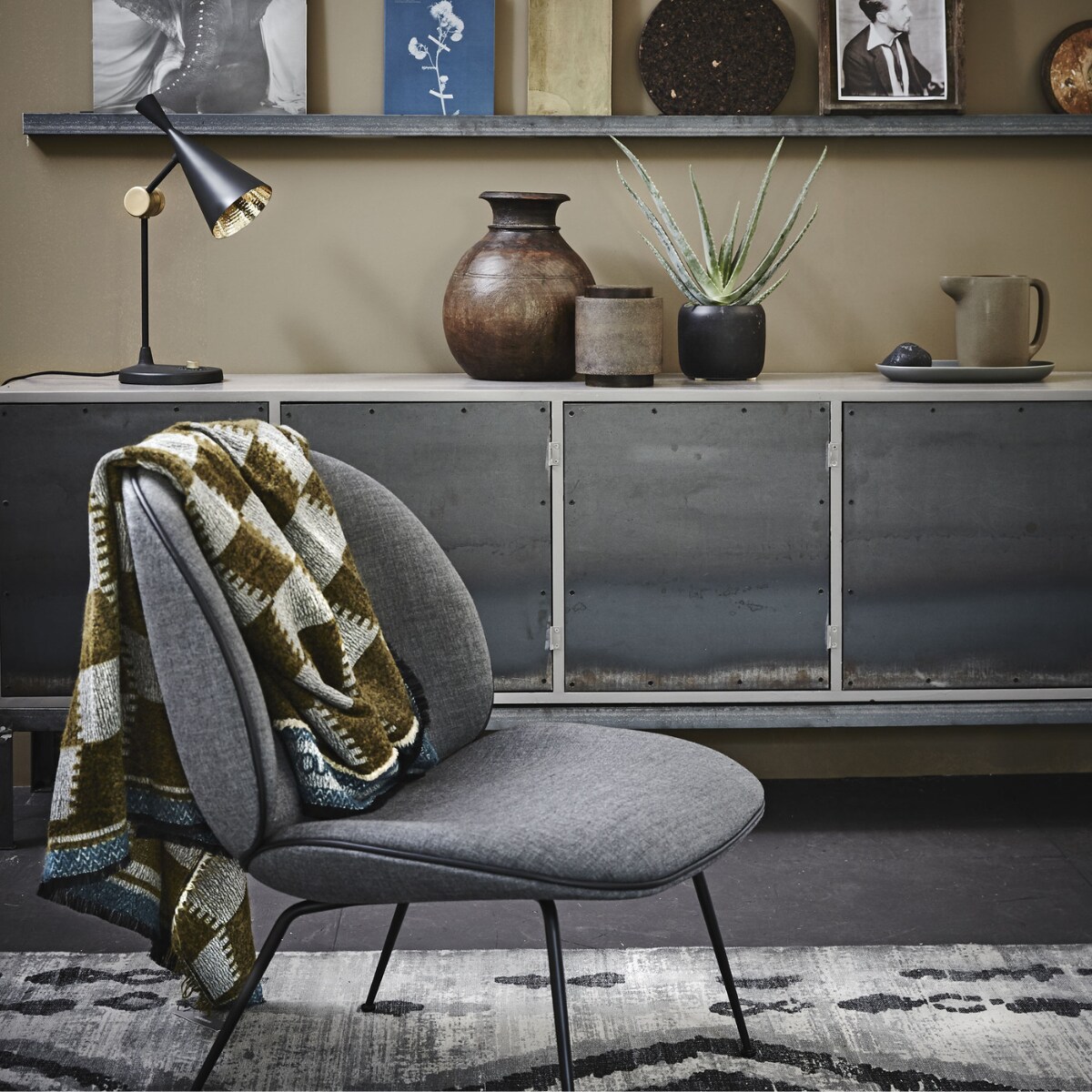 Dressoir met stalen deuren (Combitex). Fauteuil van Gubi (Mobilia). Sjaal van Humanoid (Sukha Amsterdam). Grijze kelim van HKliving (vtwonen.nl). Op de rand: papieren zak met olifant van Love Warriors (Couleur Locale), boek over blauwdruk- fotografie (Matter of Material), messing dienblad (Six and Sons), onderzetter van kurk � 30 cm (Ikea), laatje met foto (Six and Sons). Op het dressoir: lamp Beat van Tom Dixon (Nordic New), houten waterkruik uit India (Couleur Locale), bruine pot (Six and Sons), zwarte bloempot, kan van aardewerk, bord Sittning uit set van drie (Ikea). Muurverf Mexican Sand van Pure &amp; Original (De Ru). vtwonen 10-2015 | styling Cleo Scheulderman | Fotografie Alexander van Berge
