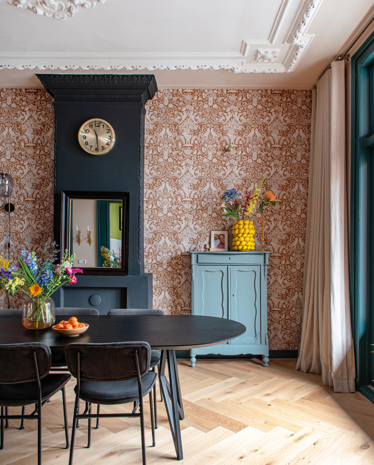 Behang en gordijnen Karwei, klok Karlsson, eettafel Studio Henk, stoelen Wonenmetlef, vaas Des Pots, vintage kast geschilderd in Livid van Little Greene, wandlamp Marktplaats. Muurverf schouw Off-Black van Farrow & Ball, muurverf plafond IG KH M-058 van Karwei. Visgraatparket Blank Geolied Eiken van vtwonen via Karwei. Overig onbekend. vtwonen 09-2023 | productie De Binnenkijkers | styling Jeske Weel | fotografie Caroline Coehorst
