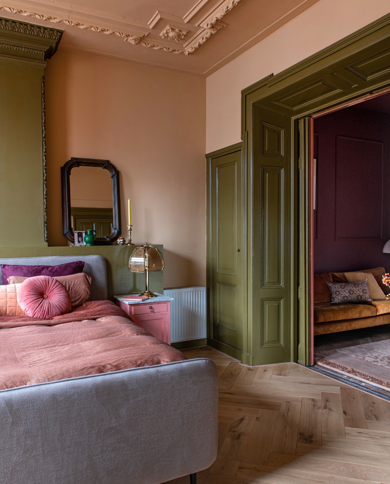 Verf houtwerk en schouw Hunter, muurverf Teddy en verf vintage nachtkast Electric Pink van Lab Paint. Bed Swiss Sense, dekbedovertrek Beddinghouse, rond kussen en geel kussen Essenza. Bank Sofacompany, gebloemd kussen Karwei, vloerkleed BePureHome. Spiegel, tafellamp en kandelaar vintage. Visgraatparket Blank Geolied Eiken van vtwonen via Karwei. Overig onbekend.