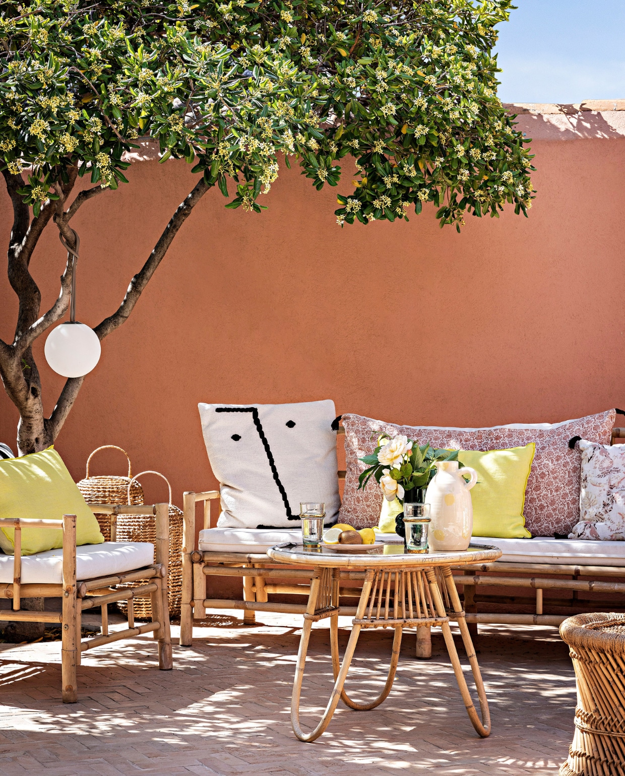 Ambachtelijke bejmattegels Art et Sud. Muren geschilderd met leemverf Terre Rose van Ressource. Bank en fauteuil Decoclico. Zitkussens Ambiance et Matières, kussen zwarte streep Maison Madeleine, gele kussens Maison de Vacances, bloemenkussens Cyrillus. Rotan tafel erfstuk. Gele kan Oustao. Hanglamp Fatboy. Rotan lantaarns en Marokkaanse kruk Jiji La Palme d’Or. vtwonen special binnenkijken 06-2023 | productie &amp; styling Marie Maud Levron | fotografie Yann Deret