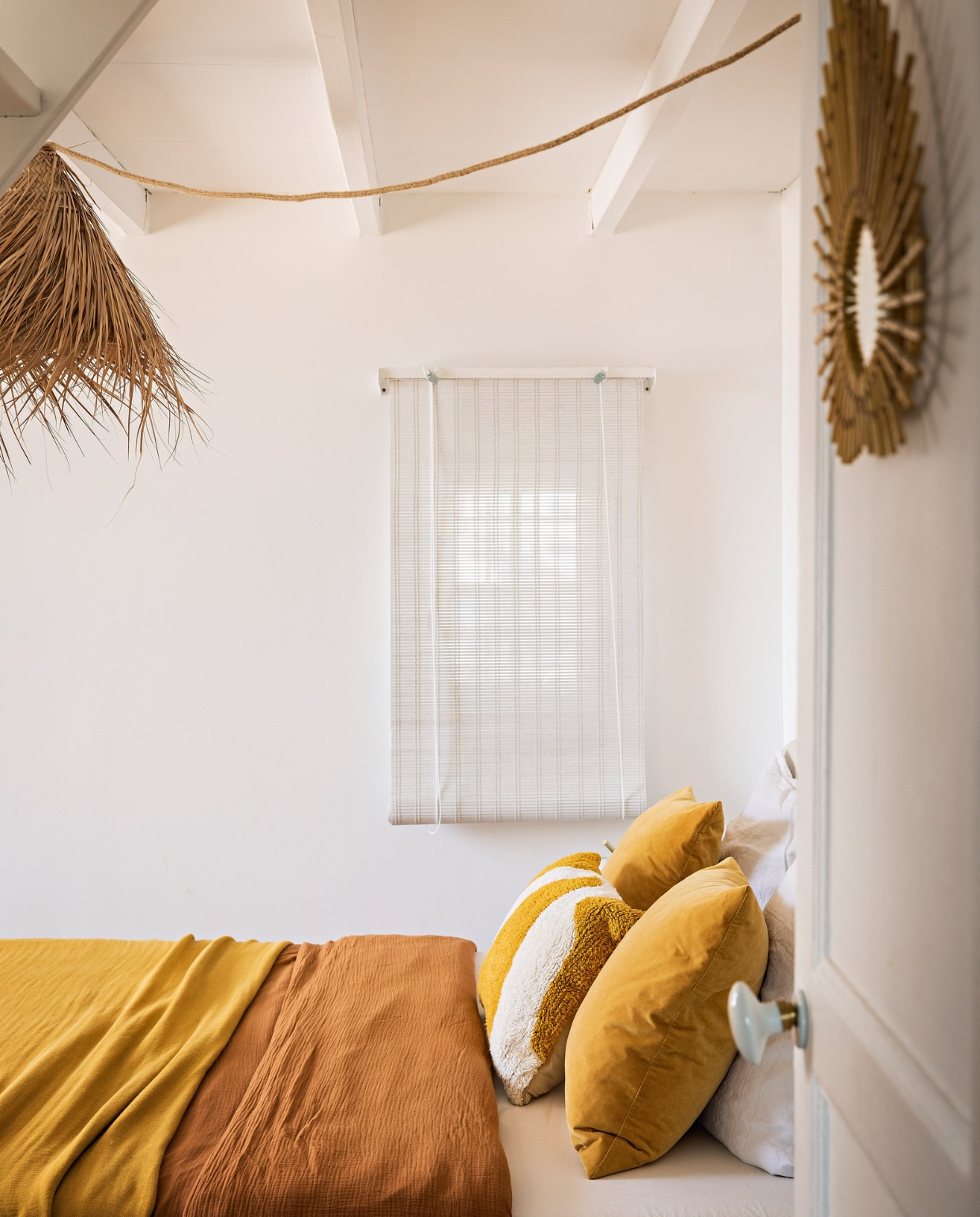 Plaid en dekbedovertrek La Redoute. Gestreept kussen Monoprix, gele kussens Ikea. Hanglamp Jiji La Palme d’Or. Rotan spiegel Bon Coin. Raambekleding Haomy. vtwonen special binnenkijken 06-2023 | productie &amp; styling Marie Maud Levron | fotografie Yann Deret