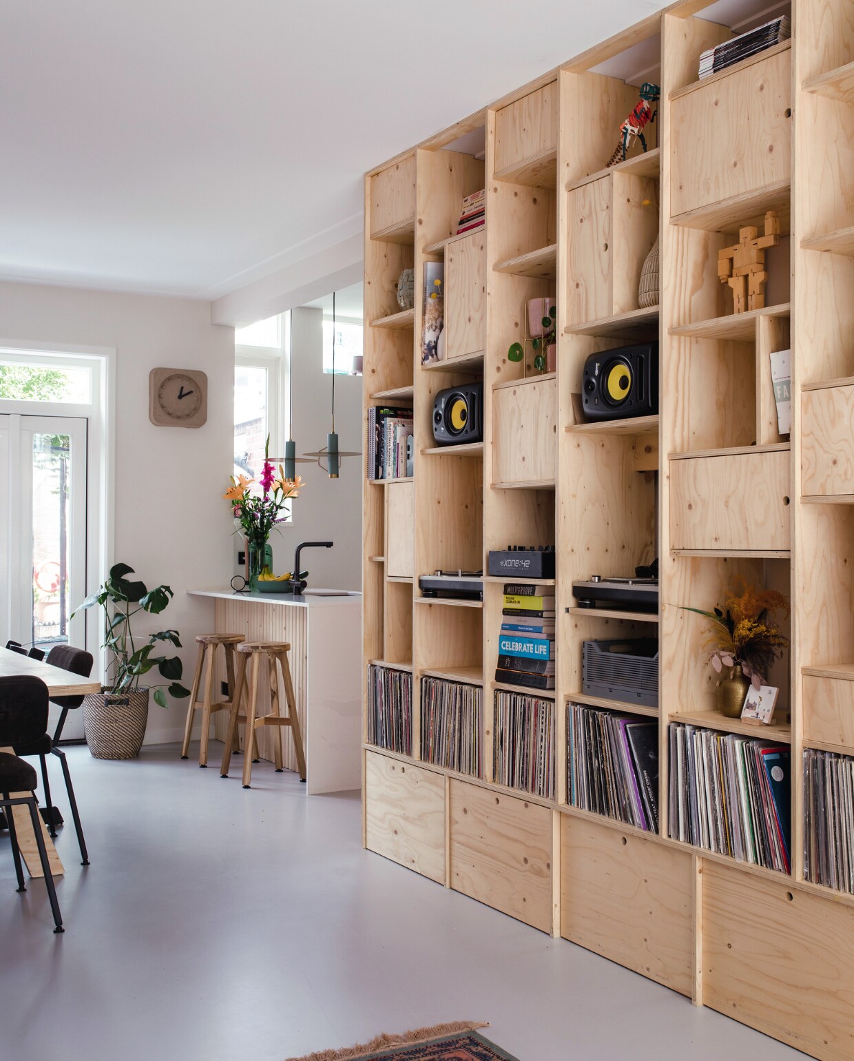 Wandkast gemaakt door Danijel Vidic, speakers Rokit van Krk Systems, houten robot Cubebot van Areaware, roze plantenpotten Hema, gietvloer Drt Gietvloeren, plantenmand Rågkorn en barkrukken van Ikea. Klok Pulp Time van Zuiver, tafel Piet Hein Eek, stoelen Studio Henk, hanglampen Lucide, vaas Bloomingville, schaal Casa. vtwonen 09-2023 | styling Luka Jacobs | fotografie Corine hoge Bavel-Jansen