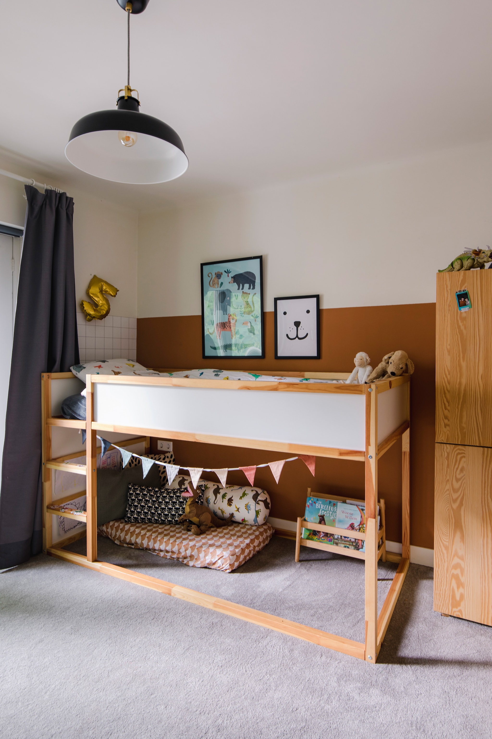 Bed Kura, hanglamp Ranarp, kast, zwart-wit kussen, rolkussen en boekenrek Flisat Ikea. Muurverf in Spiced Honey van Flexa. Gordijn van vorige bewoners. Overig onbekend. vtwonen 09-2023 | styling Luka Jacobs | fotografie Corine hoge Bavel-Jansen