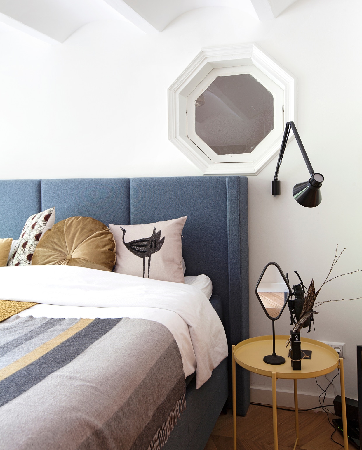 Bed Swiss Sense. Gestreepte deken John Hanly &amp; Co Ltd. van de Bijenkorf. Kussen met stippen, rond kussen, kussen met vogel, spiegel en kunstwerk op bijzettafel Kieveen. Gele bijzettafel Ikea. Wandlamp herkomst onbekend. vtwonen binnenkijken special 12-2020 | Fotografie Corine Hoge Bavel | Styling Sheila Sletbeen via Kieveen