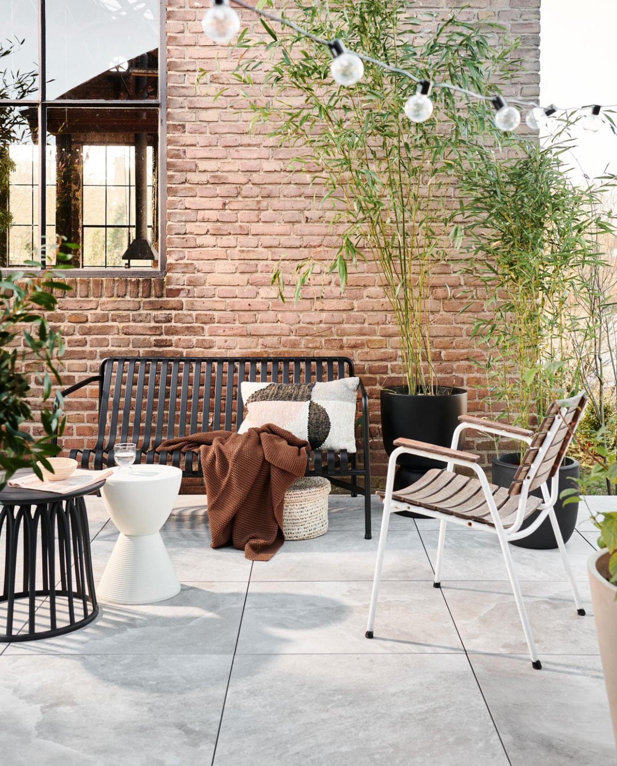 Kruk Kartell. Deken Marc O’Polo. Kussen Bloomingville. Lichtsnoer vtwonen. Hoge pot op voet Elho. Lage zwarte pot Capi. Boy bijzettafel zwart basiclabel.nl). Mand anders.com. Stoel vandijkenko.nl. Buitentegels Uni Dark Travertine, 70x70x3,2 cm per m² € 74,95 Solostone. vtwonen special tuin 6 | styling Marlies Does | fotografie Sjoerd Eickmans