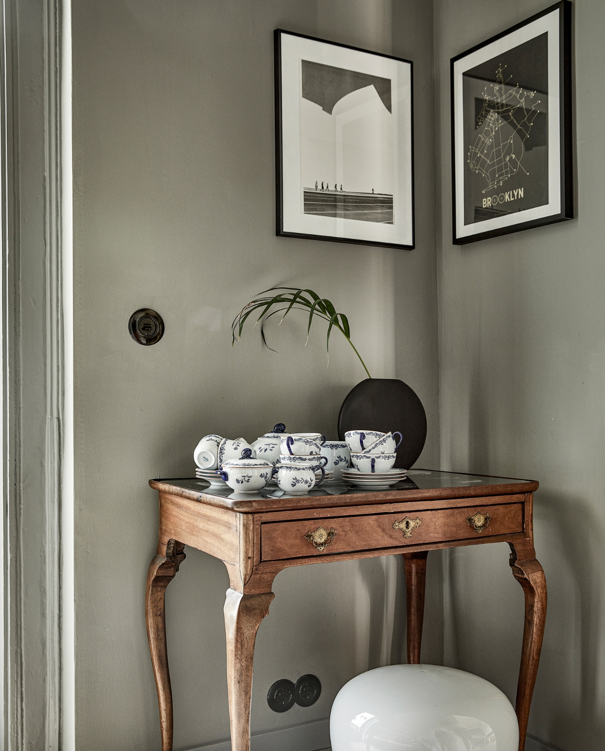 Bakelieten schakelmateriaal De Oude Schakelaar. Prints aan de muur meegenomen van reizen. Lijsten en bollamp Ikea. Antieke theetafel en Ostindia-servies van R_rstrand erfstuk. Zwarte vaas gekregen. vtwonen  binnenkijken special 03-2022 | productie &amp; styling José Martens | fotografie Peggy Janssen