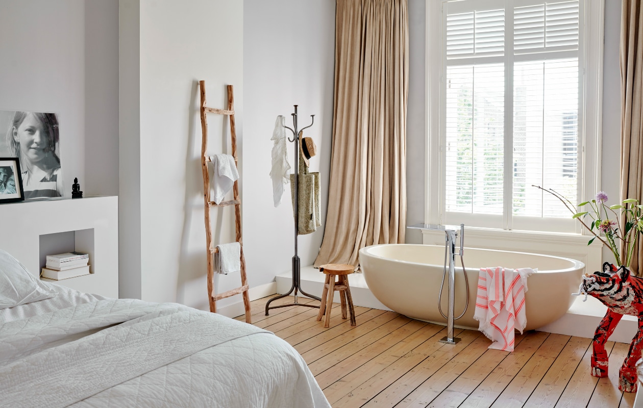 Het bad in de slaapkamer is zo bedacht door de vorige eigenaars. De vloer is geschilderd met traplak, waardoor hij tegen een stootje kan. De linnen gordijnen en shutters werden overgenomen van de vorige bewoners. De tijger van papier-mach_ is gemaakt door dochter Roos. Ladder van Atelier 8, kapstok en krukje Homestock. Hamamdoek Hema. vtwonen 04-2020 | productie Features &amp; More | styling Wilma Custers | fotografie Renee Frinking