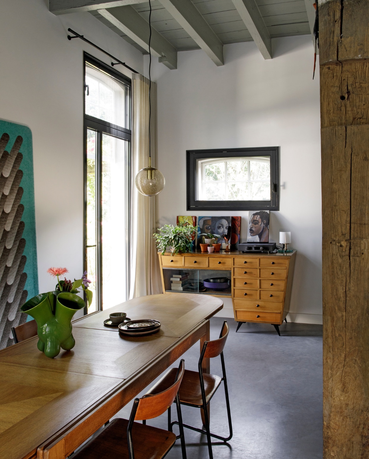 Eettafel, eetkamerstoelen, ladekast en hanglamp Morentz. Groene vaas Roderick Vos, aardewerk Claudy Jongstra. Gordijnen eigen ontwerp. Kunstwerken uit Nigeria. Herkomst bloempotten en lamp onbekend. vtwonen 10-2020 | fotografie Inga Powilleit | styling José Martens