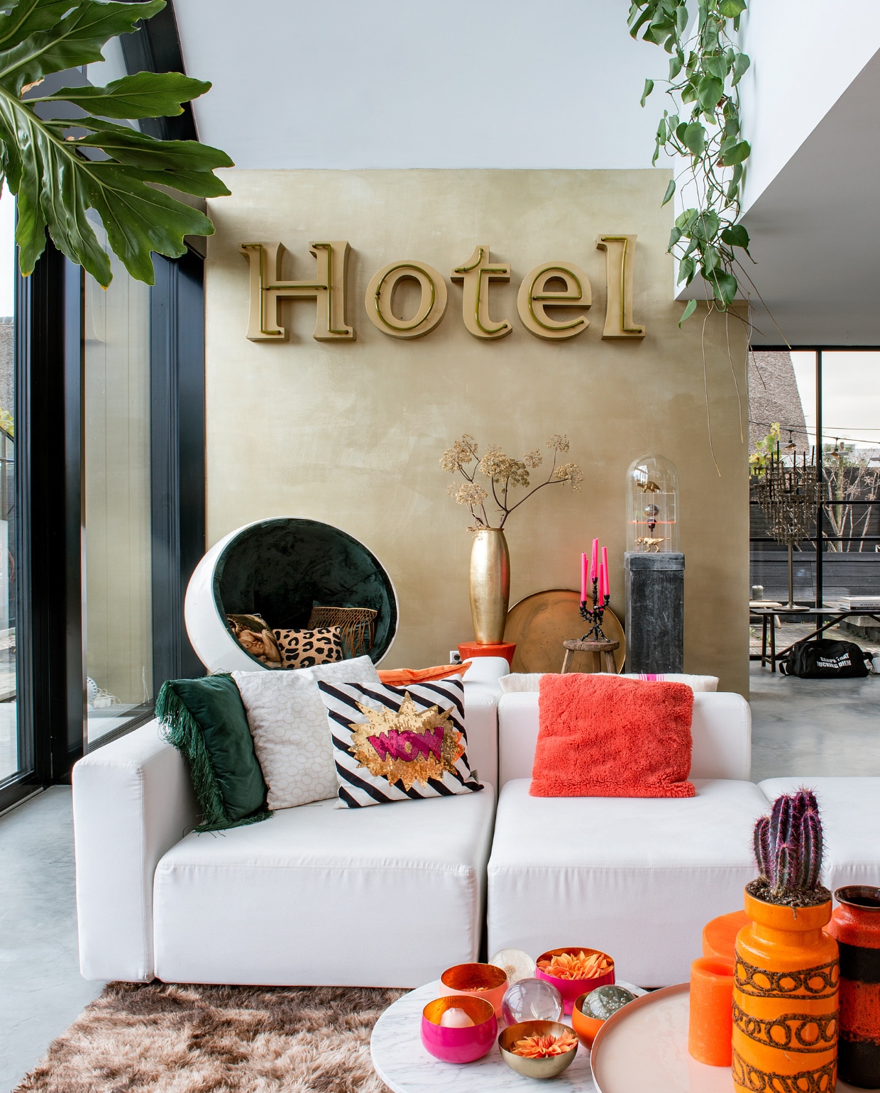 Bank Moduplus, roze bijzettafel Karwei. Kussens en houten blok Nijhof. Stoel Lodge Living, vitrinekast Ikea, vacht Vachten van Terschelling. Roze en oranje kommen en planten De Kaardebol. Oranje hoofd met hoed en oranje vaas links Eigenaar 8. Lamp en aardewerken vazen vintage. Gietvloer Willem Designvloeren, muurverf Blossom Pink van Le Noir &amp; Blanc. Overig onbekend. vtwonen 10-2023 | fotografie Ton Bouwer
