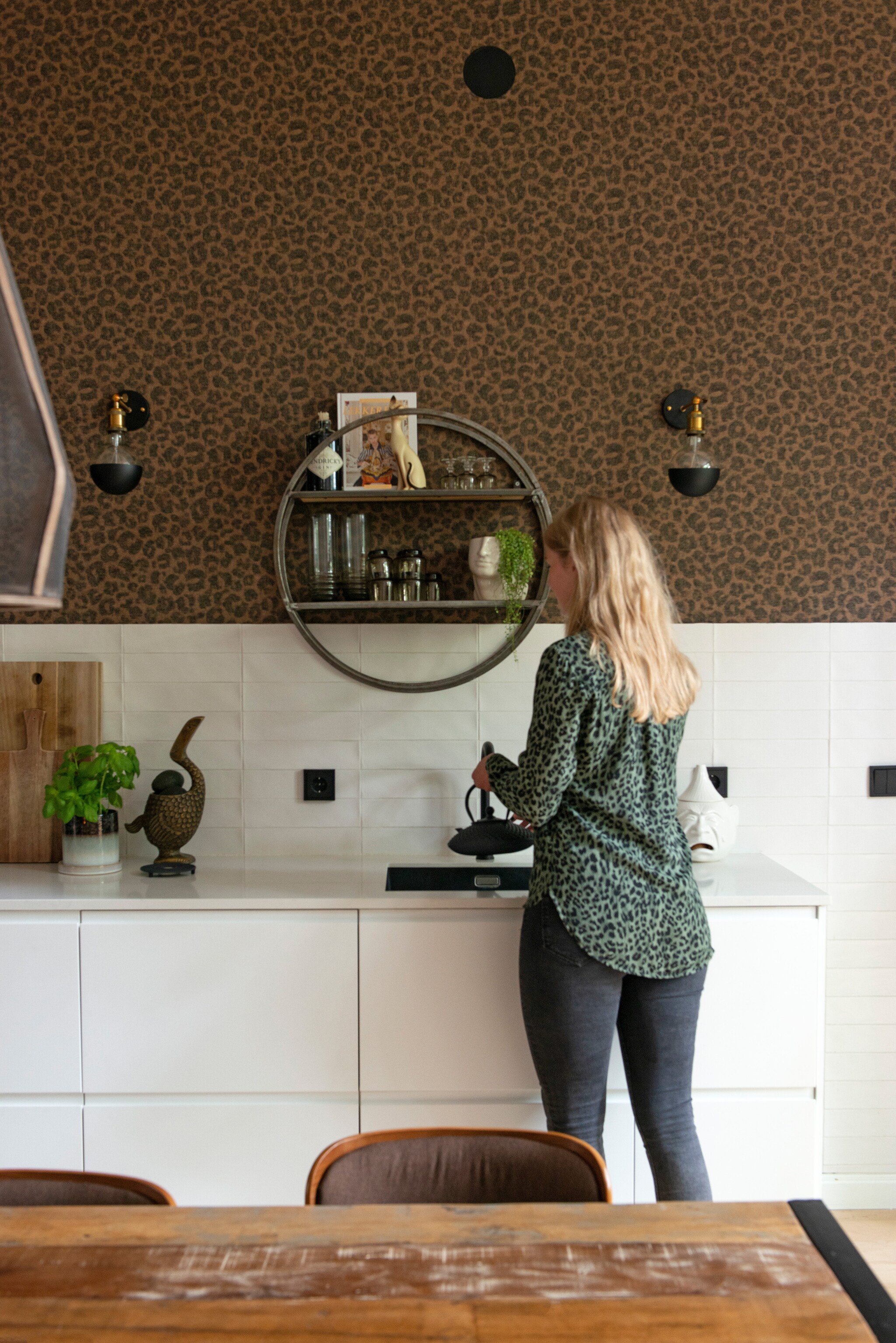 Keuken Ikea, composiet blad met marmerlook 123werkbladen. Tegels Friese Witjes, soortgelijke bij Harlinger Aardewerk &amp; Tegelfabriek. Behang Cheetah van BN Walls. Wandlampen Foir. Wandkast vintage vondst, uienpot en glaswerk kringloop, bloempot hoofd H&amp;M Home. Snijplank Ikea, object vogel Sissy-Boy, theepot Bredemeijer. Tafel Giga Meubel, stoelen Dutchbone. vtwonen 01-2021 | styling Jeske Weel | fotografie Caroline Coehorst