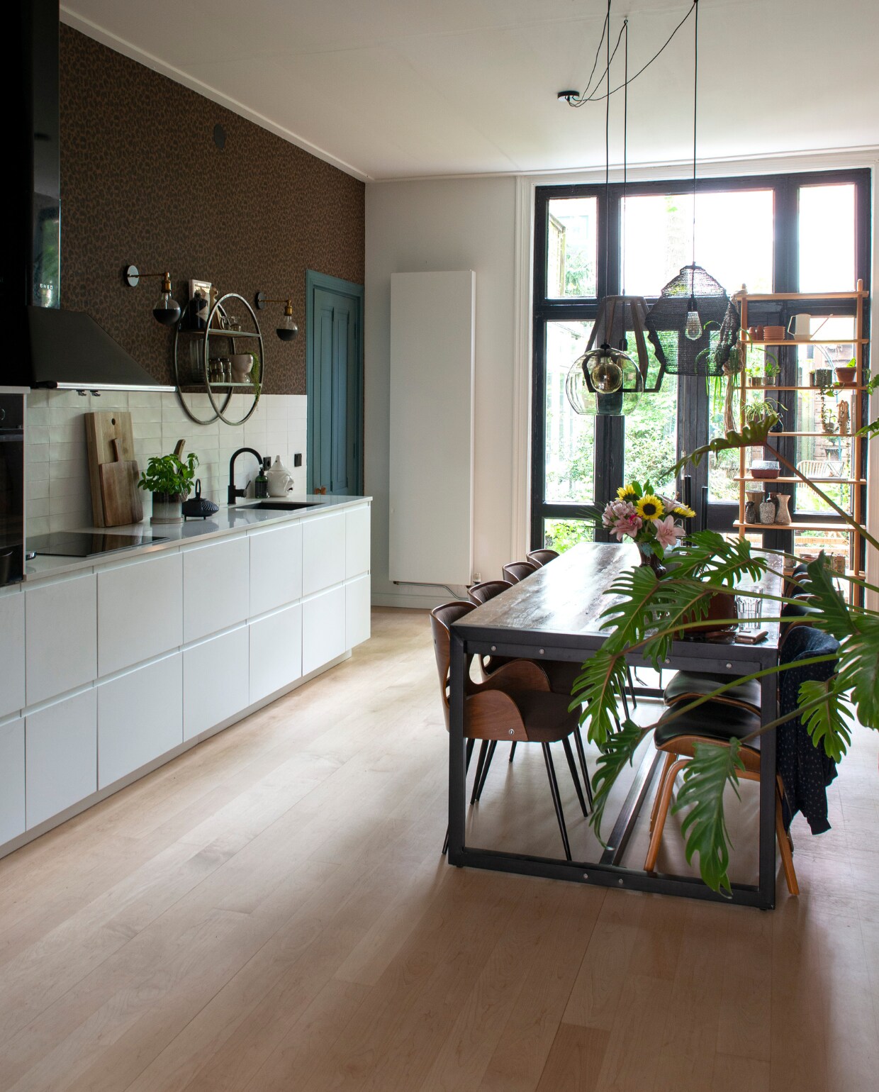 Keuken Ikea. Tegels Friese Witjes, soortgelijke bij Harlinger Aardewerk &amp; Tegelfabriek. Behang Cheetah van BN Walls. Wandlampen Foir. Wandkast vintage vondst, uienpot en glaswerk kringloop. Verf deur Inchyra Blue van Farrow &amp; Ball, muurverf verkeerswit Ral 9016. Snijplank Ikea, object vogel Sissy-Boy, theepot Bredemeijer. Tafel Giga Meubel, stoelen Dutchbone, hanglampen en bloempot Kwantum. De esdoornhouten vloer die er al lag is opgeschuurd en gelakt. vtwonen 01-2021 | styling Jeske Weel | fotografie Caroline Coehorst