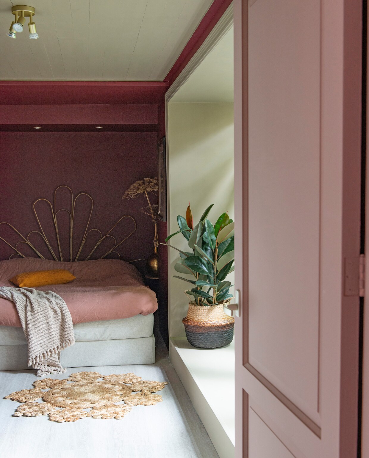 Muurverf Preference Red Estate Emulsion en lak Mouse’s Back Dead Flat van Farrow &amp; Ball. Bed Ikea, bedwand zelfgemaakt van bamboe plantensteunen. Kussen en plaid Sissy-Boy. Mand Praxis, met rubberplant. Vloer restpartij van winkel die niet meer bestaat. Vloerkleed garage sale. Bijzettafel Kwantum, tak berenklauw, herkomst pot onbekend. Debbie spoot de lamp die er al hing goud. vtwonen 01-2021 | styling Jeske Weel | fotografie Caroline Coehorst