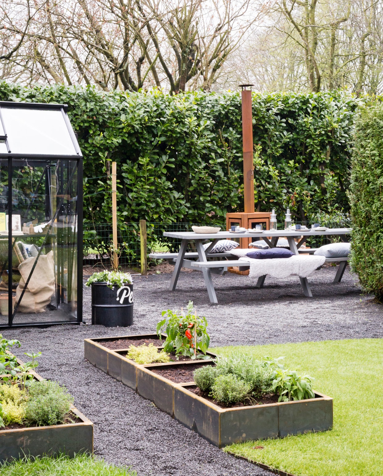 Zwarte tuinkas Birdlip 84, met veiligheidsglas € 1599,-, met daarin tafel Birdlip 84  € 259,- (royalwellkassen.nl). Grind Basalt split, per m³ € 124,-, met daaronder splitplaten Eurogravel, per m² € 12,50 (amagard.com). Kunstgras Royal Grass Sense met ReaDY technologie, per m² € 39,95 (royalgrass-kunstgras.nl). Moestuinbakken met kantopsluiting van cortenstaal, prijs op aanvraag (greenmaxx.eu). Kruidenplantjes en groente, vanaf € 1,-, kussen Denim met rafelrand € 25,- (leurs.nl). Vachtjes € 9,95 (ikea.nl). Uni Kussen Havana Blue € 18,95, dessin kussen Sara Blue € 19,95 (Hartman.nl). Kussen Denim Blue van By Mölle, 55x55 cm € 52,-, lantaarns van Household Hardware, per stuk € 14,95, rechthoekige blauwe bordjes van Merci by Serax € 15,40, bekers van Merci by Serax (vtwonen.nl).Schaal Jute € 19,95 (zusss.nl). Jutenzak in de kas, prijs op aanvraag, DIY: olieton wordt plantenbak (livingonce.nl). Buitenhaard Quaruba XL, met aan vier zijden glas, op verplaatsbaar plateau € 1375,- (reny.nl). Schutting privébezit, gebeitst met pantserbeits Antraciet 1216, per 2,5 liter  € 51,99, picknicktafel privébezit, gebeitst met vintage pantserbeits Stoer Antraciet 1148, per 750 ml € 14,95 (rambo.nl). Servies op tafel van de kringloop vtwonen weer verliefd op je tuin 2 | styling Leonie Mooren | fotografie Barbara Kieboom