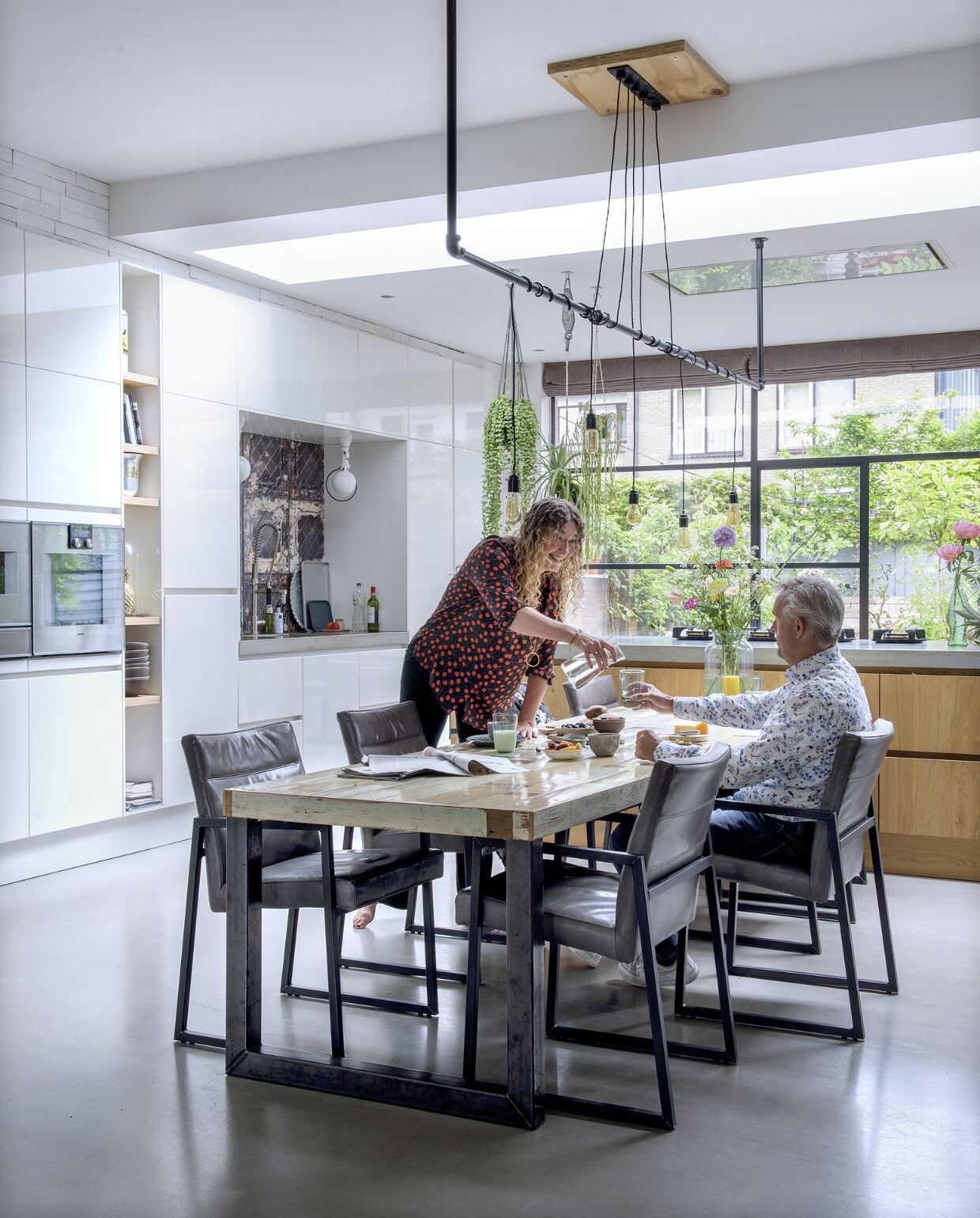 De oorspronkelijke woonkamer, keuken en dichte aanbouw zijn doorgebroken tot een leefruimte met een ruime keuken, eettafel en zithoek, een stalen pui opent naar de tuin. De tafel is op maat gemaakt door Maatmeubelen ’s-Hertogenbosch, de stoelen zijn van Seven Days, de lamp is gemaakt door Koos, met gordijn-roedes van Ikea; inspiratiebron was de toonbanklamp die ze zagen bij een slager in New York. vtwonen 01-2019 | fotograaf Ton Bouwer | styling Wendy Romeijn en Monique van der Pauw