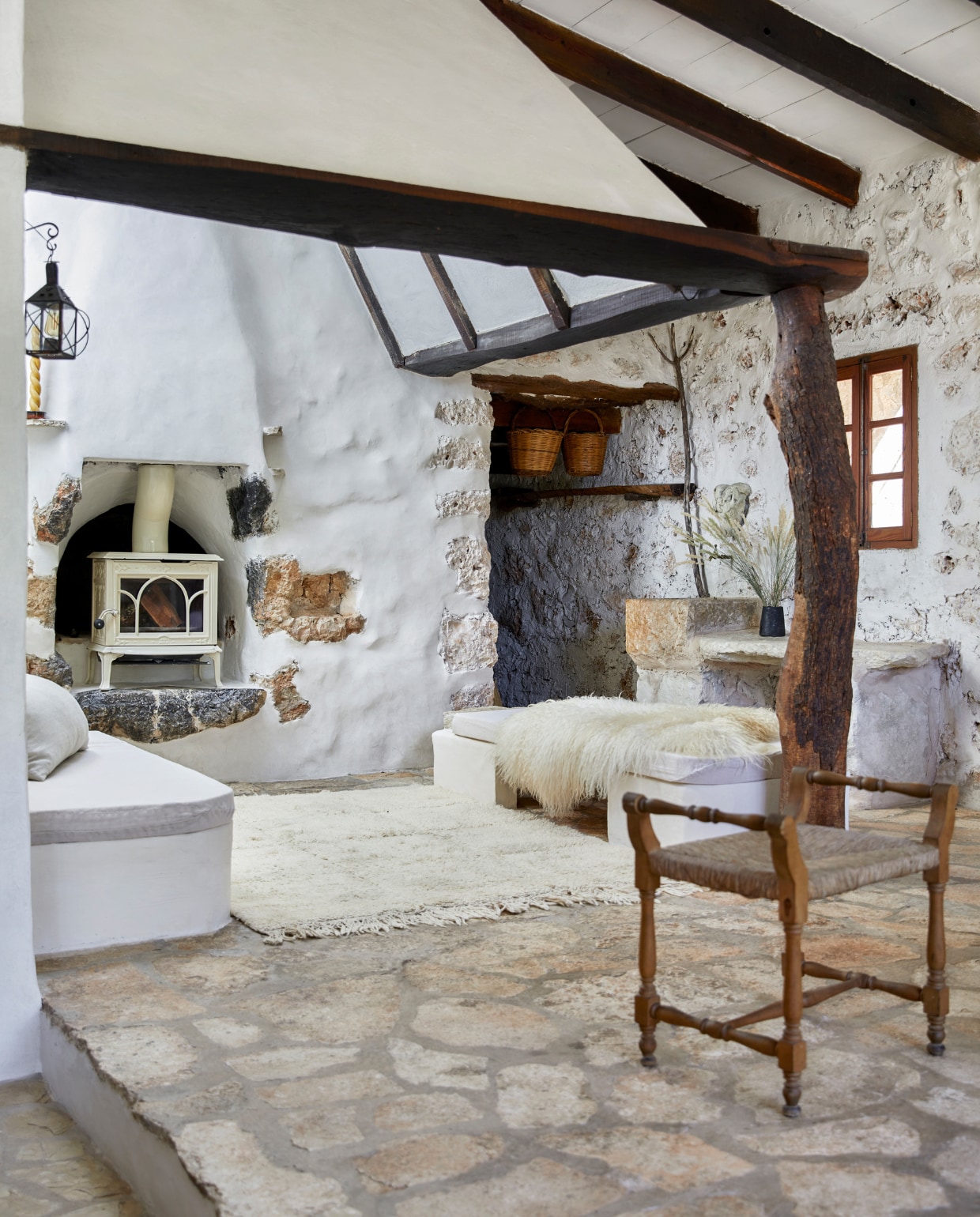 Op de ingebouwde banken liggen schapenvachten uit Ierland. Houtkachel Jotul. De originele muren zijn deels afgewerkt met tadelakt. Vloerkleed uit Marokko. Stoel en wandlamp waren al in het huis. Manden lokaal gekocht. Vaas uit eigen atelier. vtwonen special binnenkijken 06-2023 | productie Bureaux/Living Inside | fotografie Greg Cox