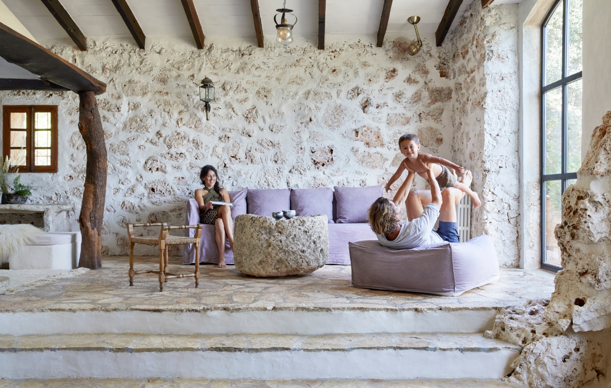 Hanglamp traditioneel Mallorcaans. Wandlamp en stoel al aanwezig. Bank en poef Gervasoni. Salontafel zelfgemaakt van een uitgeholde steen die vroeger werd gebruikt om druiven te pletten. Keramiek uit eigen atelier. vtwonen special binnenkijken 06-2023 | productie Bureaux/Living Inside | fotografie Greg Cox