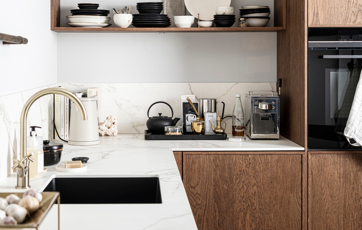 Keuken Dark Oak zoals getoond, exclusief accessoires € 19.950,- | M.m.v zarahome.com (opbergpot en bord met bordenstandaard), casagitane.com (schaal op poot), vtwonen.nl (glazen en servies van vtwonen), sjostrandcoffee.nl (koffiezetapparaat en melkopschuimer), vtwonen.nl (dienblad en theepot van Serax, waterkoker Sowden van Hay), thefinestore.com (dienblad). Overig privébezit. vtwonen 12-2021 | productie Tanja Saarberg | styling Kim van Rossenberg | fotografie  Sjoerd Eickmans