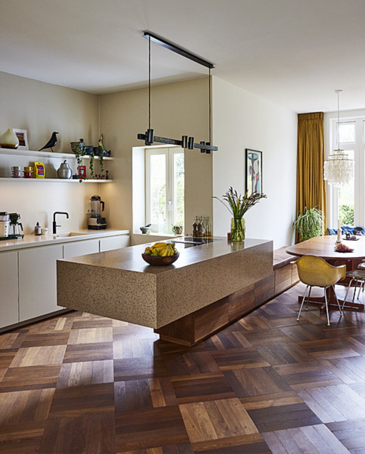 Ontwerp keuken, kookeiland en houten wandbanken X+L, uitvoering Schriever Interieurbouw. Materiaal kookeiland Durat van PyraSied. Fruitmand, vaas, peer, vis, eettafel en kandelaars vintage. Kraan Quooker. Vintage stoelen en vogel Eames. Leren kussen en gordijn Links &amp; Co. Hanglamp boven aanrecht Sofisticato van Koen Van Guijze, hanglamp Verner Panton. Zeefdruk Andreas Samuelsson. Overig onbekend. vtwonen 11-2023 | styling Mariella Kallenberg | fotografie René Mesman