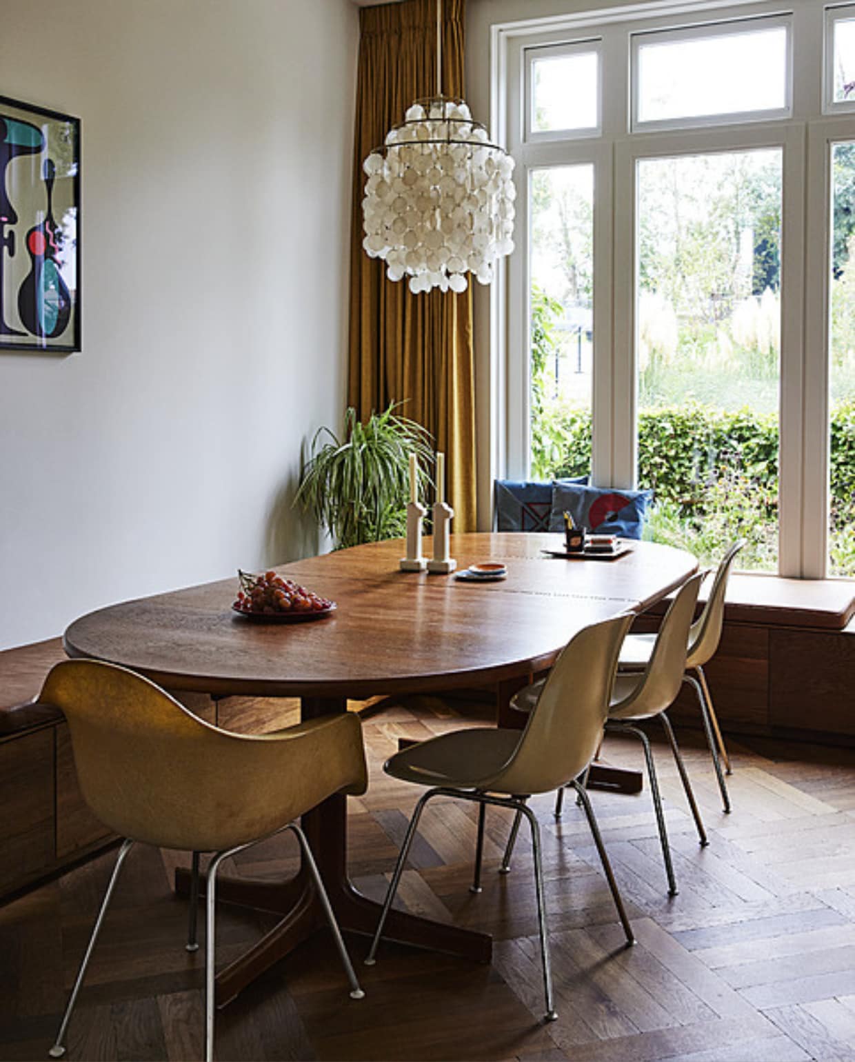 Eettafel en kandelaars vintage. Vintage stoelen Eames, lamp Verner Panton, bakjes op tafel cadeau, bord met pennen rommelmarkt, kussens zelfgemaakt, zeefdruk Andreas Samuelsson, vloer Wolfsburg van Urbanwood van Martijn de Wit Vloeren. Gordijn Links &amp; Co. vtwonen 11-2023 | styling Mariella Kallenberg | fotografie René Mesman