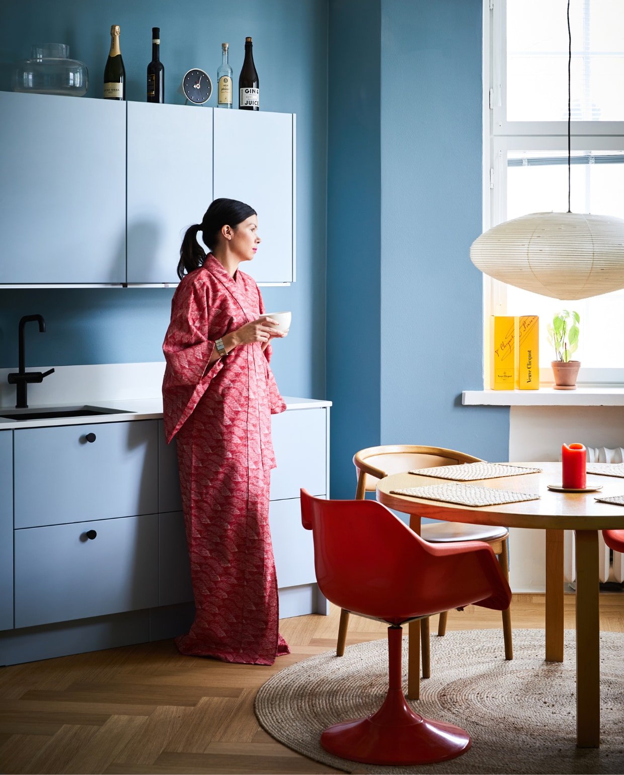 Ook de keuken kreeg een lichtblauwe tint. Eettafel en placemats Artek. Vintage oranje stoel Robin Day voor Hille. Houten stoel Mama Hakola. Klok en lamp Akari Vitra. Vloerkleed Anno. vtwonen special binnenkijken 12-2022 | productie Living Inside | fotografie Krista Keltanen