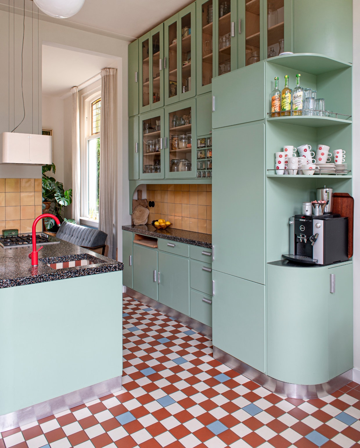 Keuken ontworpen door Studio Daan Hietbrink, verfkleur fronten Room Green 81 van Farrow &amp; Ball. Keukenblad Marcolina Terrazzo en Beton. Rode kraan sanitair.nl. Wandtegels en barkrukken Marktplaats. Vloertegels Winckelmans. Fruitschaal en broodplank uit Frankrijk. Overig onbekend. vtwonen 03-2023 | styling en fotografie Caroline Coehorst i.s.m. Studio Daan Hietbrin