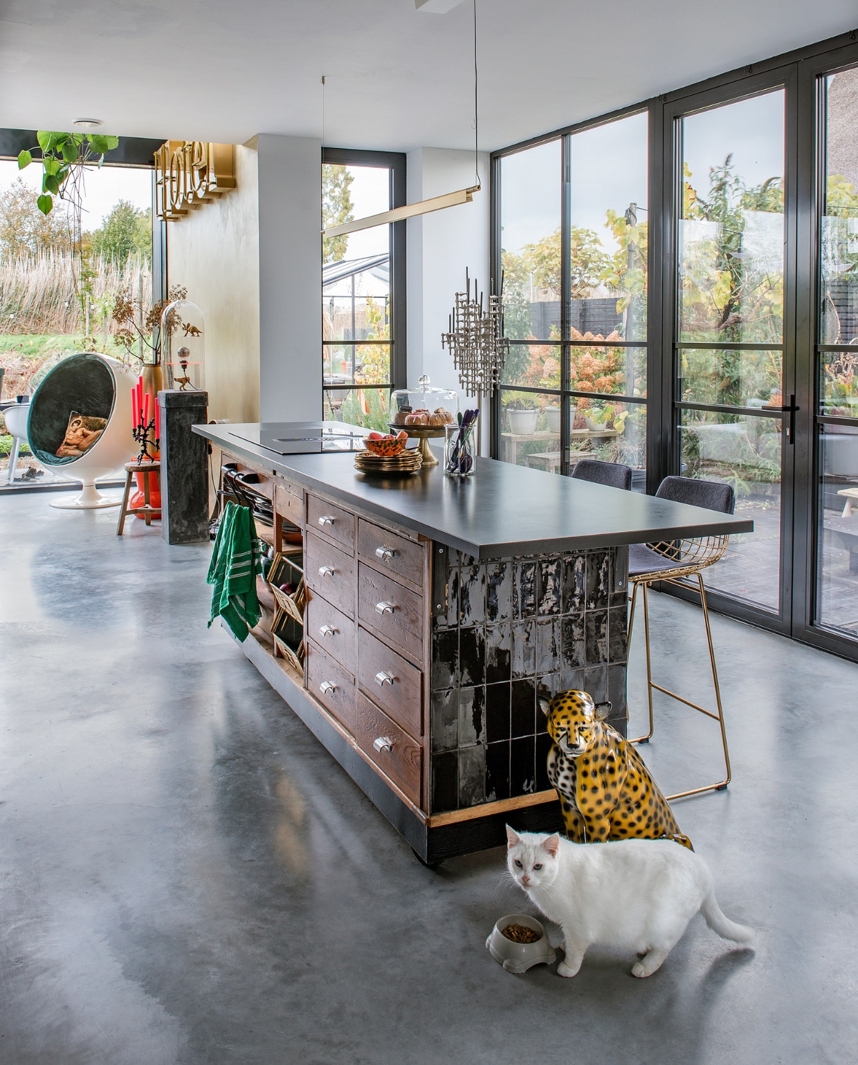 Toonbank Werkplaats 35, granieten werkblad Keukenloods, tegels Tegelsonline. Gietvloer Willem Designvloeren. Gouden borden en oranje kruk De Kaardebol. Bestek Sluiz, barkrukken HKliving, letters hotel Eigenaar 8, houten kruk Nijhof. Fauteuil Ball Chair van Eero Aarnio, kandelaar Stoff Nagel, luipaard vintage. Overig onbekend. vtwonen 11-2023 | productie De Binnenkijkers | styling Jeske Weel | fotografie Caroline Coehorst